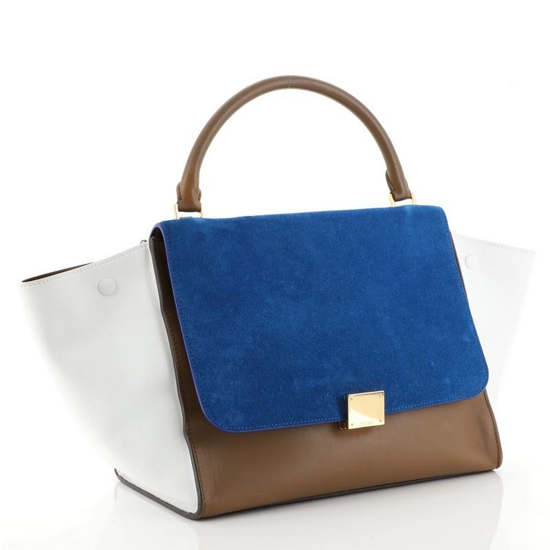This Celine Tricolor Trapeze Handbag Suede Medium, crafted from blue suede, features a rolled leather handle and gold-tone hardware. Its square flip-lock and zip closures open to a brown leather interior with slip pockets. 

Estimated Retail Price: