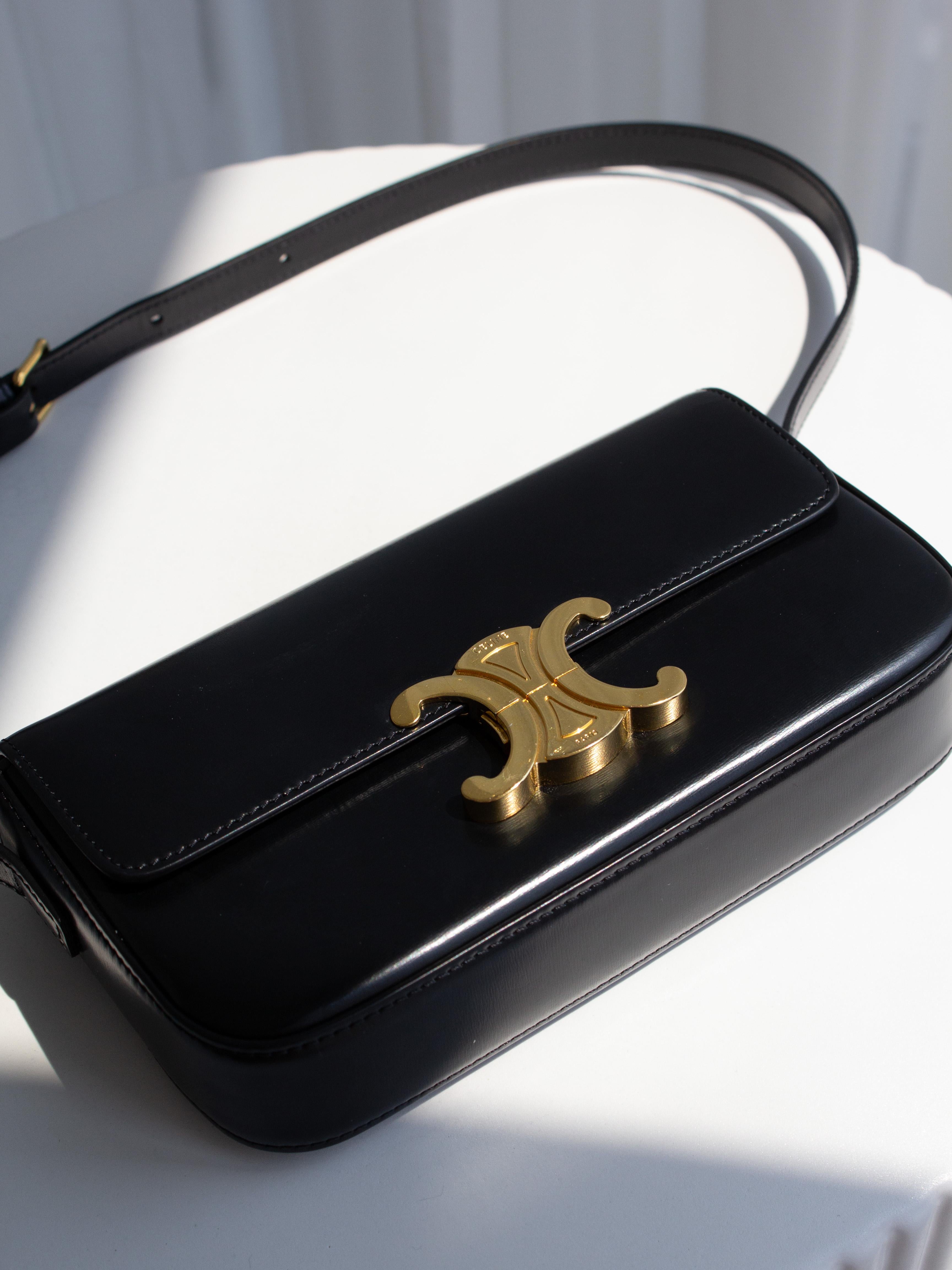 Sac Claude Triomphe de Celine en cuir de veau lisse noir avec ferrures en métal doré. Le fermoir est orné du logo iconique du Triomphe, inspiré des maillons de la chaîne de l'Arc de Triomphe. Silhouette compacte et structurée avec sangle en cuir