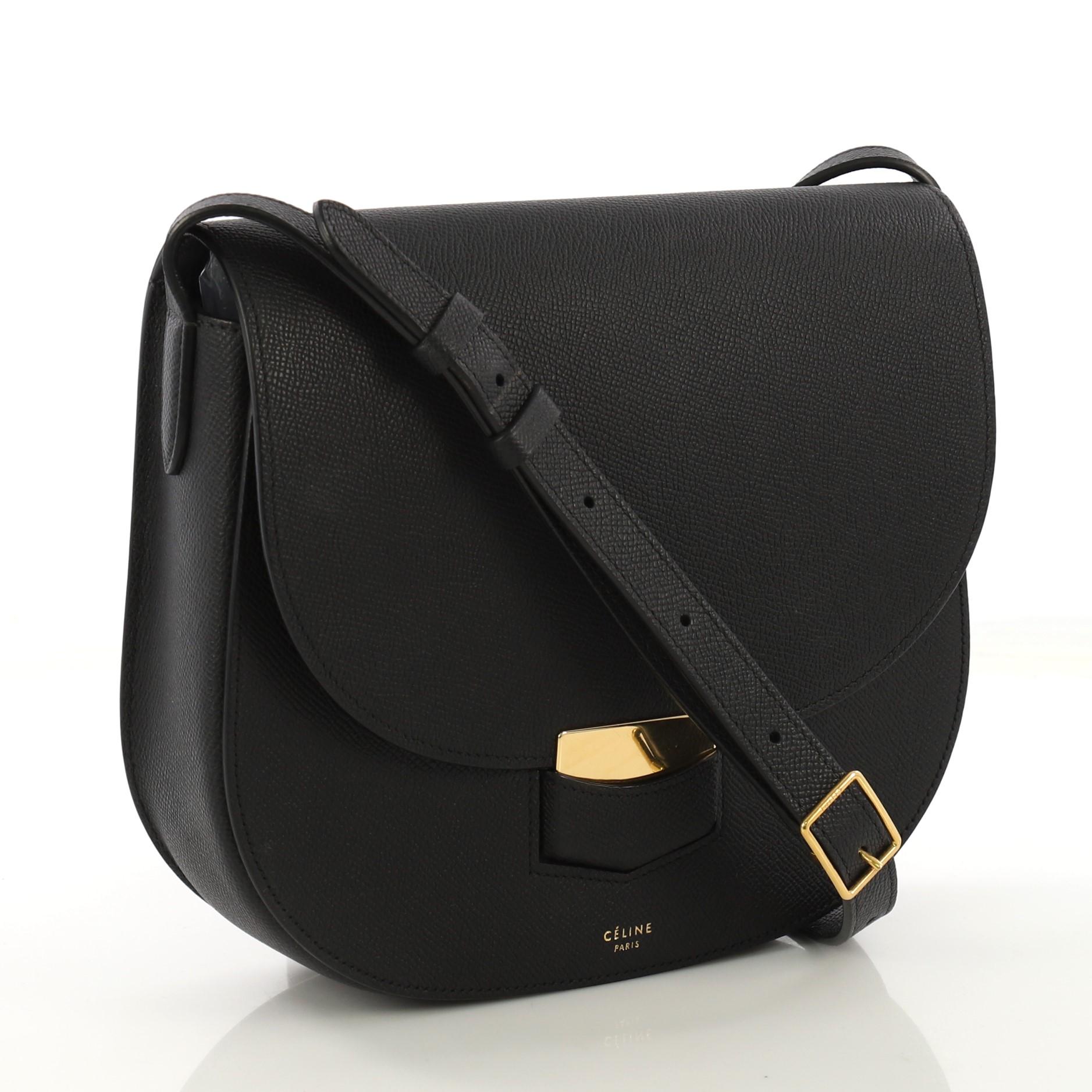 This Celine Trotteur Crossbody Bag Grainy Leather Medium, crafted from black grainy leather, features exterior back zip pocket, adjustable belted leather strap, and gold-tone hardware. Its hidden clasp closure opens to a black leather interior with