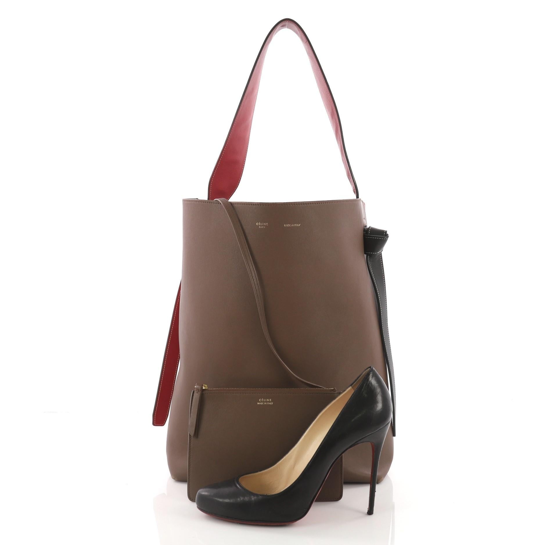 This Celine Twisted Cabas Tote Calfskin Oversized, crafted from brown and cognac calfskin leather exterior, features looping leather shoulder strap with knot ends, stamped logo at the center, and gold-tone hardware. Its wide open top showcases a