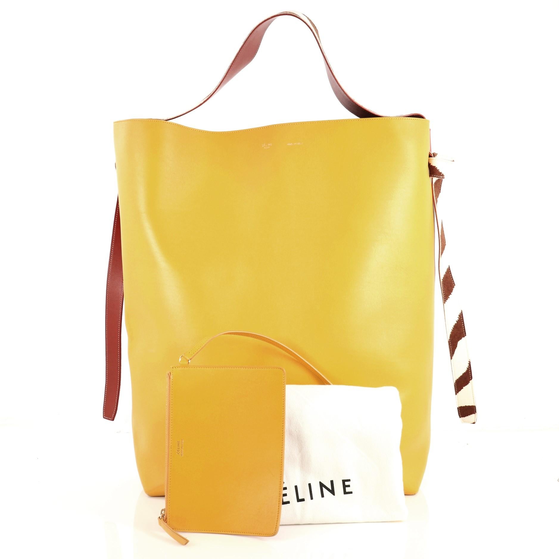 This Celine Twisted Cabas Tote Leather with Felt Oversized, crafted from red and yellow leather with zebra print felt, features looping shoulder strap with knot ends and aged gold-tone hardware. Its wide open top showcases a blue felt interior.