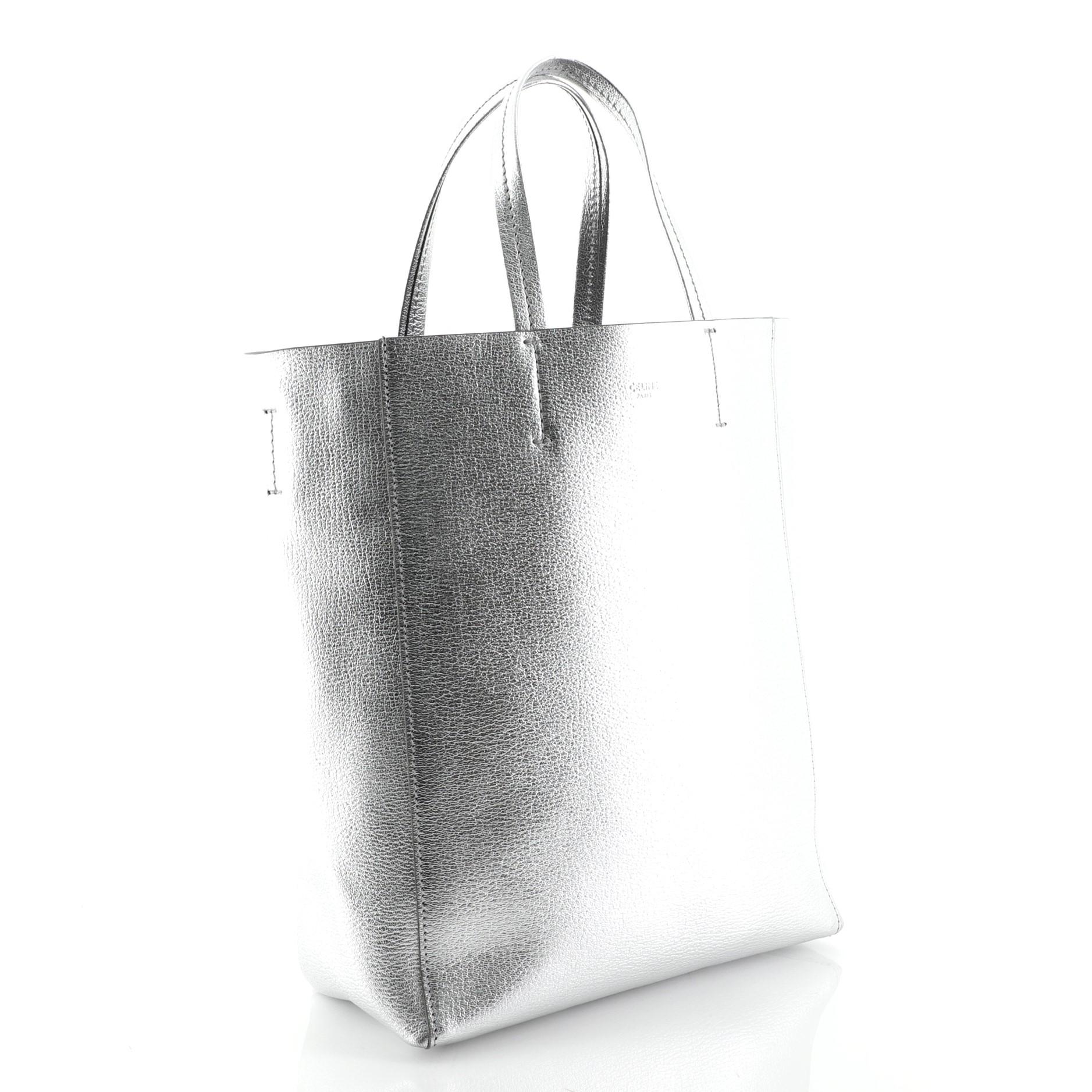 This Celine Vertical Cabas Tote Grained Calfskin Small, crafted in silver grained calfskin leather, features leather top handles, Celine stamped logo and silver-tone hardware. It opens to a black leather interior with side zip pocket. 

Estimated
