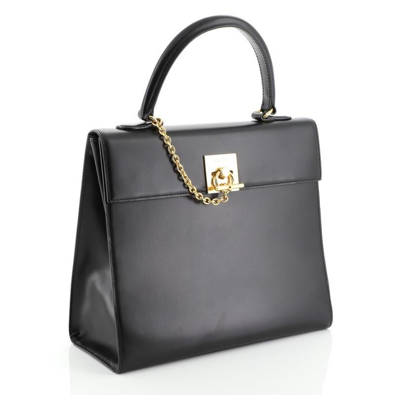 This Celine Vintage Logo Top Handle Bag Leather Small, crafted from black leather, features a rolled top handle, clasp detail with engraved 'CELINE' detail and gold-tone hardware. Its magnetic closure opens to a black leather interior with a zip