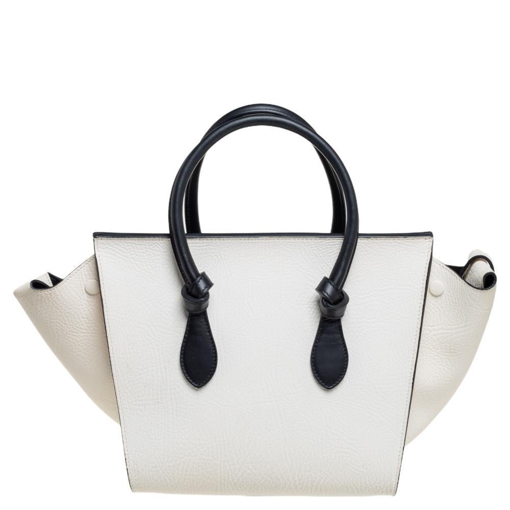 This Tie tote from Celine brings a wonderful mix of fashion and function. Expertly crafted from leather, it comes in lovely shades of black and white with dual top handles and metal studs to protect the base. Made in Italy, it has a spacious