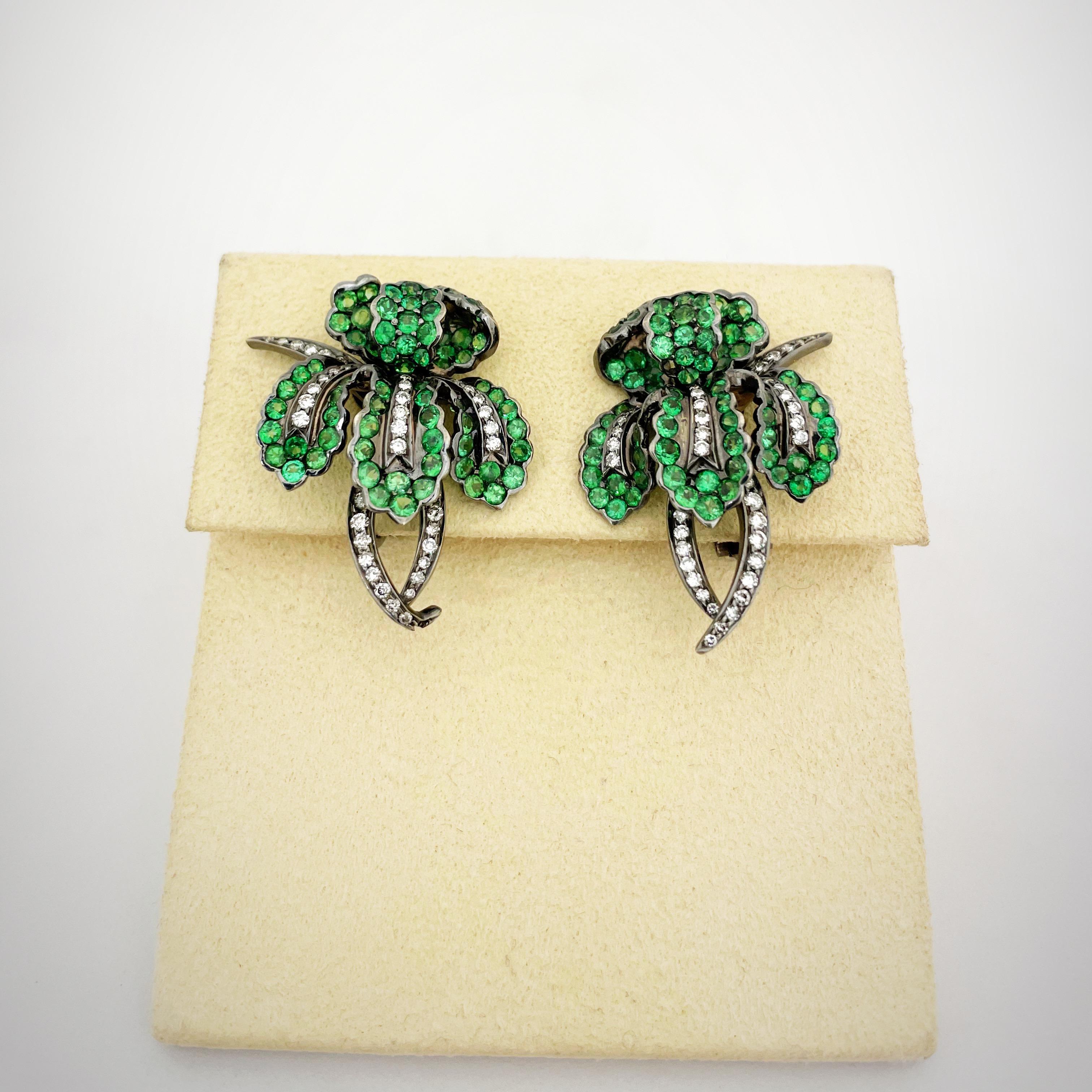 Cellini NYC beautifully crafted 18 karat gold ear clips. Green tsavorites and brilliant diamonds have been meticulously set in blackened gold for a dramatic look in these orchid flower earrings. The earrings measure 1-3/8