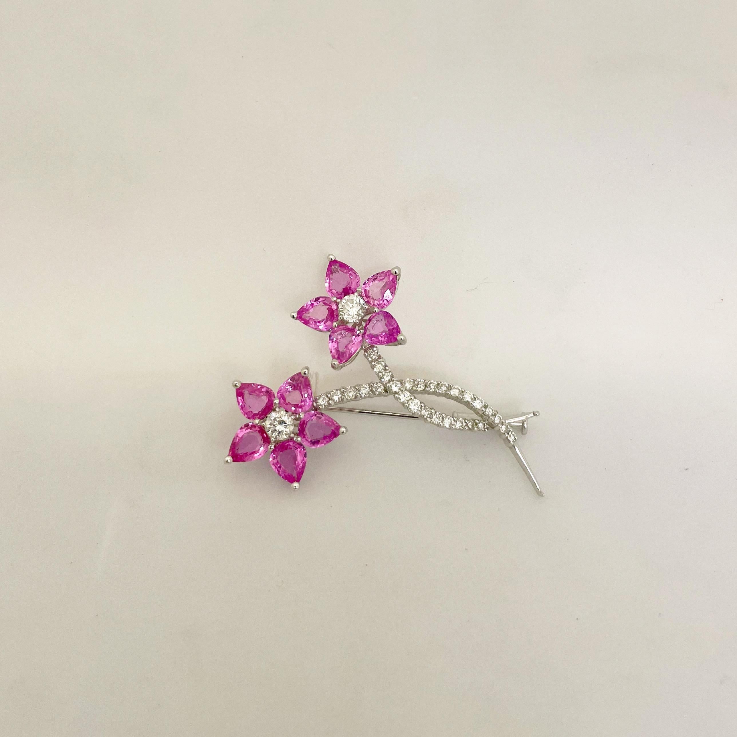 Jolie broche fleur en or blanc 18 carats. Cette broche est composée de saphirs roses en forme de poire pour les pétales. Chaque fleur a un centre en diamant rond brillant et une tige sertie de diamants ronds brillants. La broche mesure 2