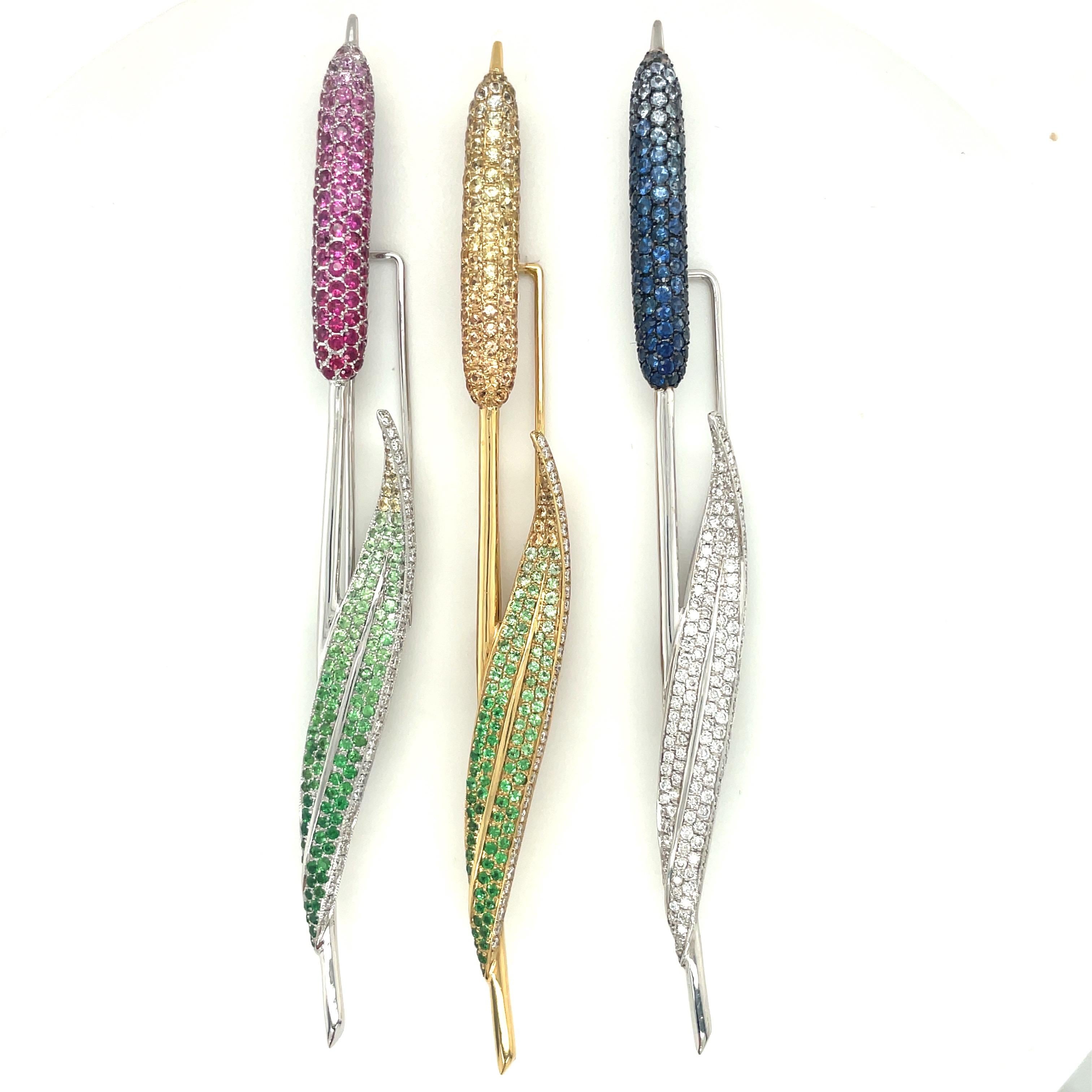 A beautiful elongated 18 karat white gold pussy willow brooch. The flower is set with ombre shades of pink sapphires.  The stem is set with round brilliant diamonds, and shades of green tsavorites. The pussy willow measures 4-5/8