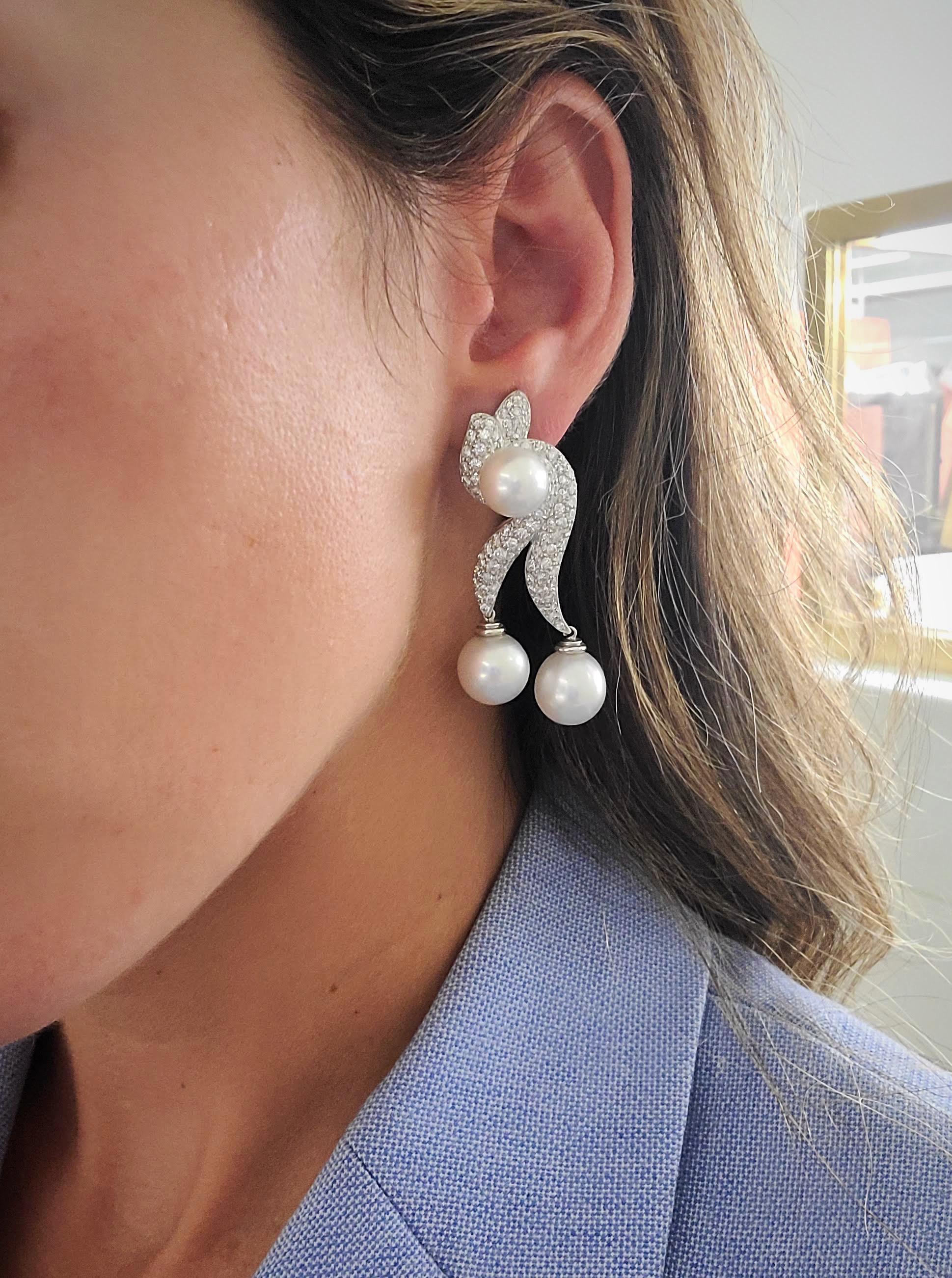 These 18 karat white gold earrings by Cellini Jewelers NYC are designed with 2 swirls set with pave Diamonds.  A South Sea Pearl sits at the center of the earring, and 2 more South Sea Pearls dangle from the bottom of the Diamond swirls. These