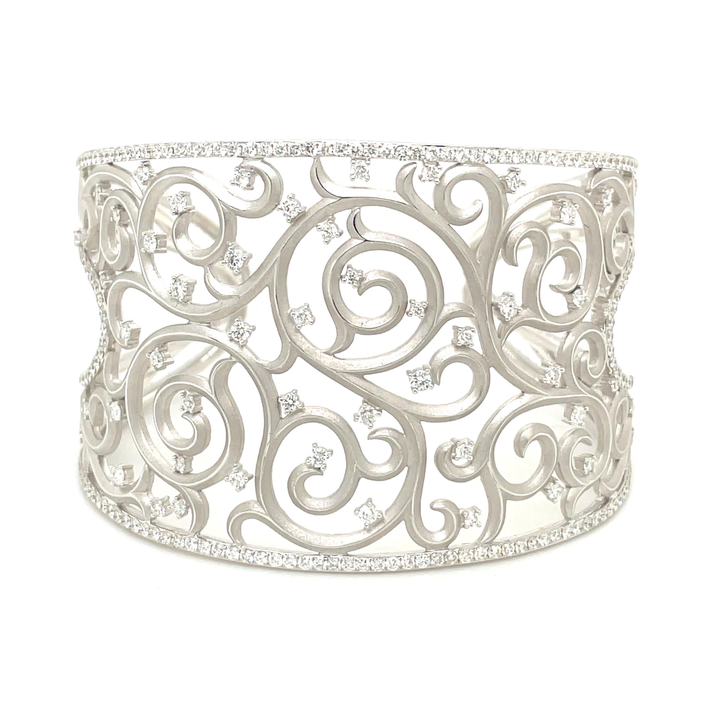 Cellini Jewelers lovely 18 karat white gold and diamond cuff bracelet. The very understated and elegant cuff is designed with a matte finished 18 karat white gold. The center is a swirl lace pattern tipped with round brilliant diamonds . A single