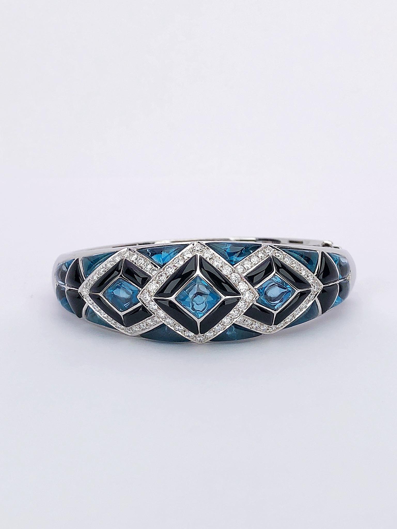 Cellini Jewelers NYC beautiful 18kt white gold bracelet is intricately set with sections of carved blue topaz and black onyx. The 3 center sections are outlined with round brilliant cut diamonds. The carved stones taper halfway down the hinged high