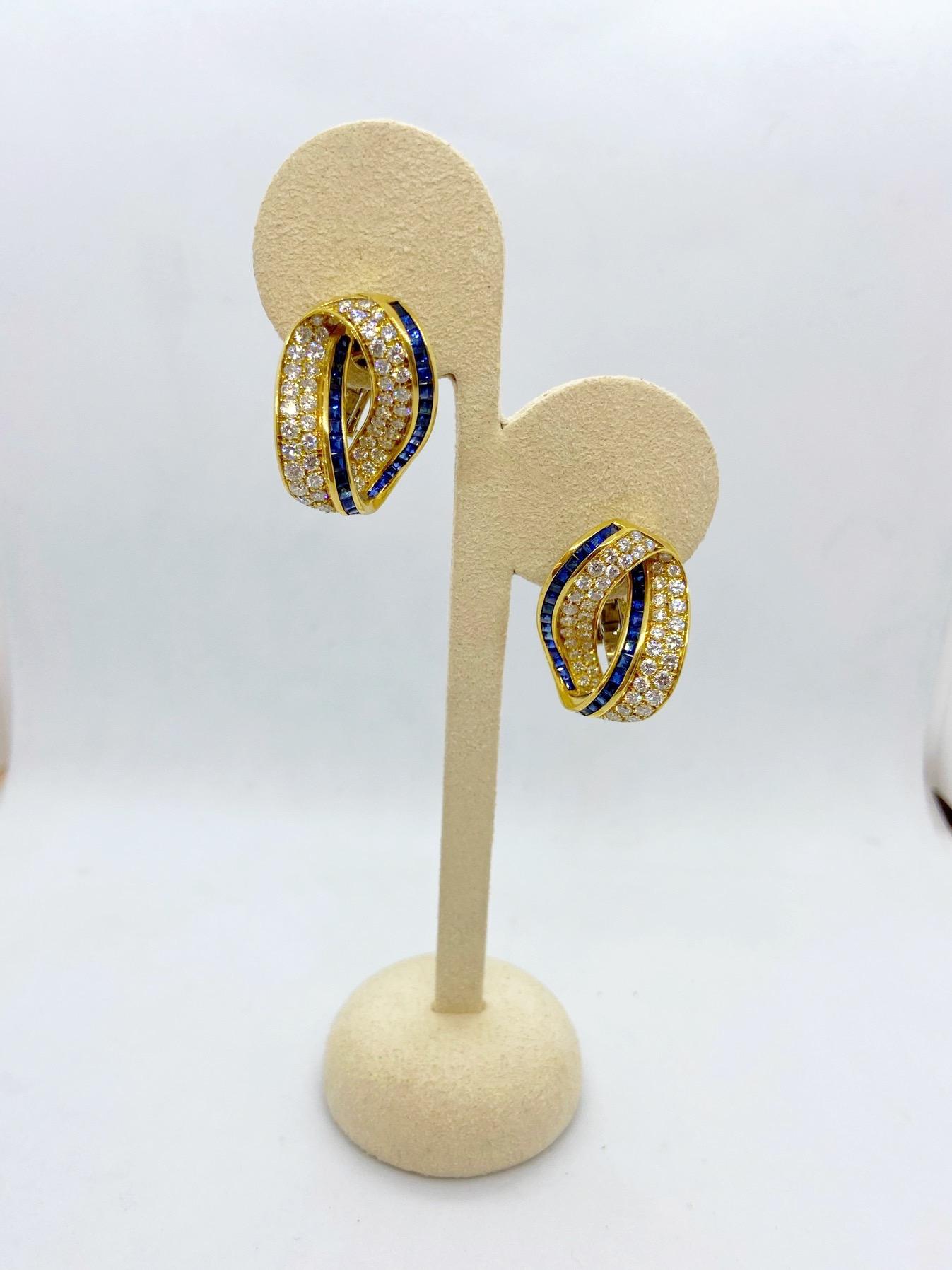 18 karat yellow gold earrings designed as an infinity knot. The earrings have been beautifully set with round brilliant diamonds and square cut blue sapphires. They have a post/clip back, and measure approximately 1