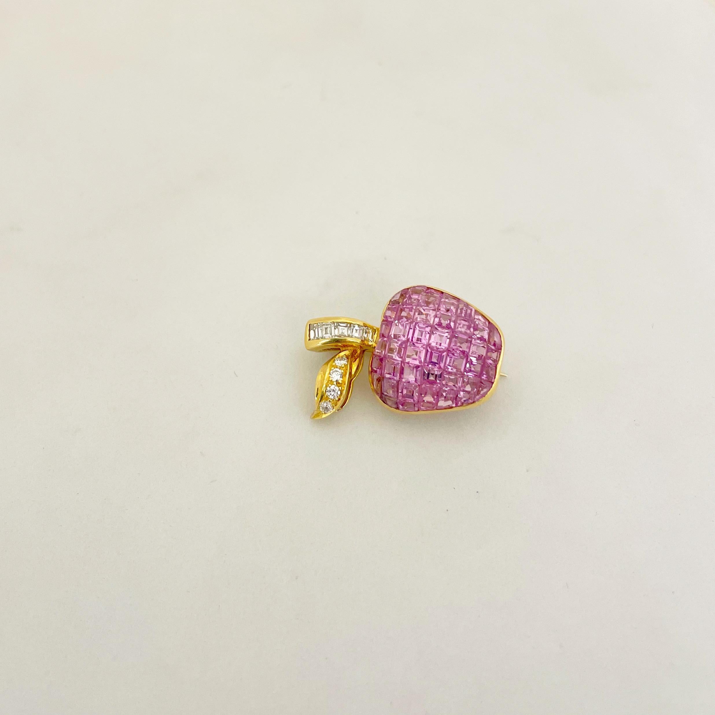 This lovely Cellini 18 karat yellow gold apple brooch has been invisibly set with vibrant square cut pink sapphires. The stem is set with square diamonds and the leaf with round brilliant diamonds. The apple measures 1