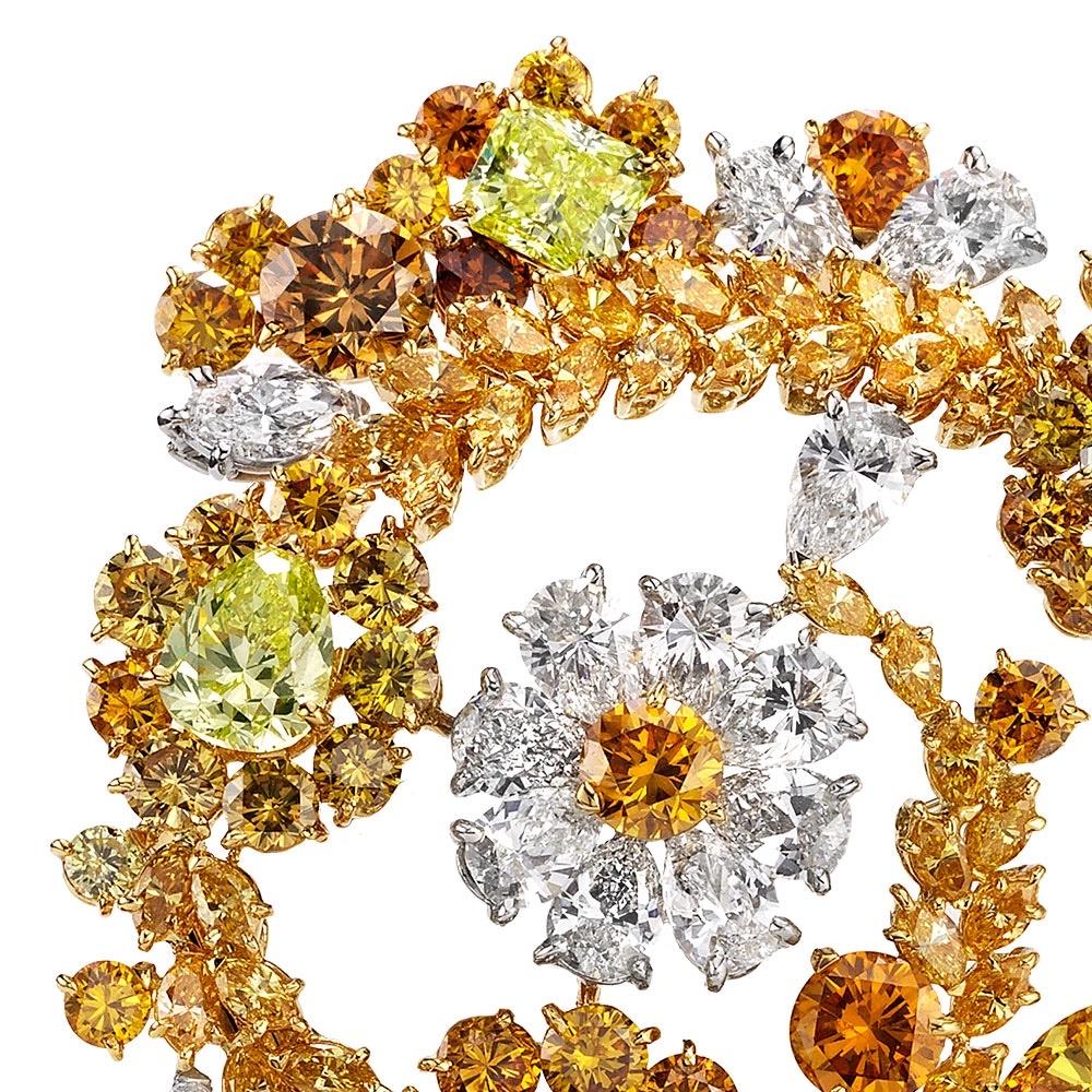 A floral spiral of varied natural fancy color diamonds in various shapes with white diamond accents. Fancy colored diamonds include yellow,orange,chartreuse, and brown. Set in 18 karat yellow and white gold. The brooch measures 2.25