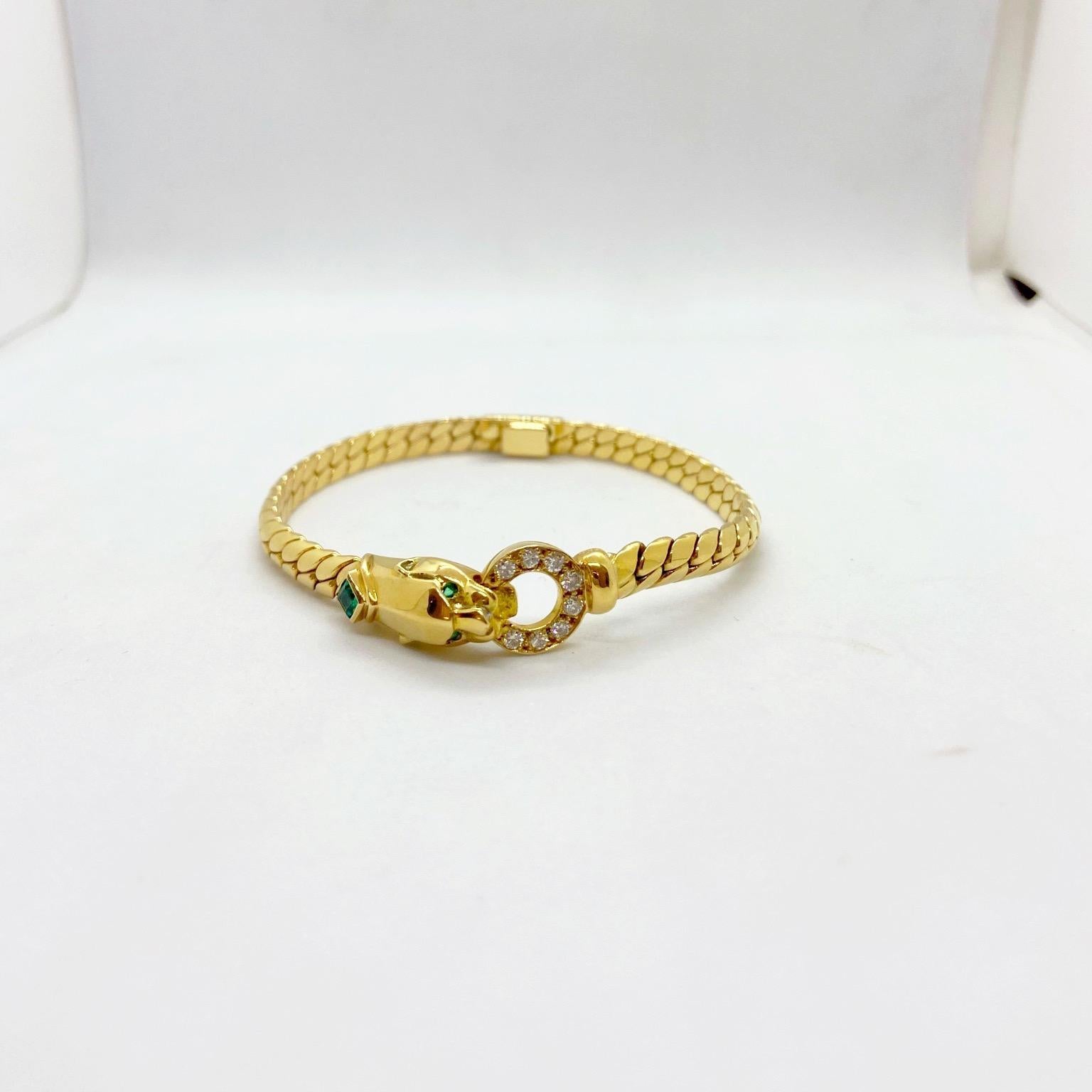 18 karat yellow gold bracelet designed with a shiny gold panther head set with emerald eyes. His neck is set with a square emerald and in his mouth he holds a diamond ring. The central motif is set in a gold link chain measuring 7.25