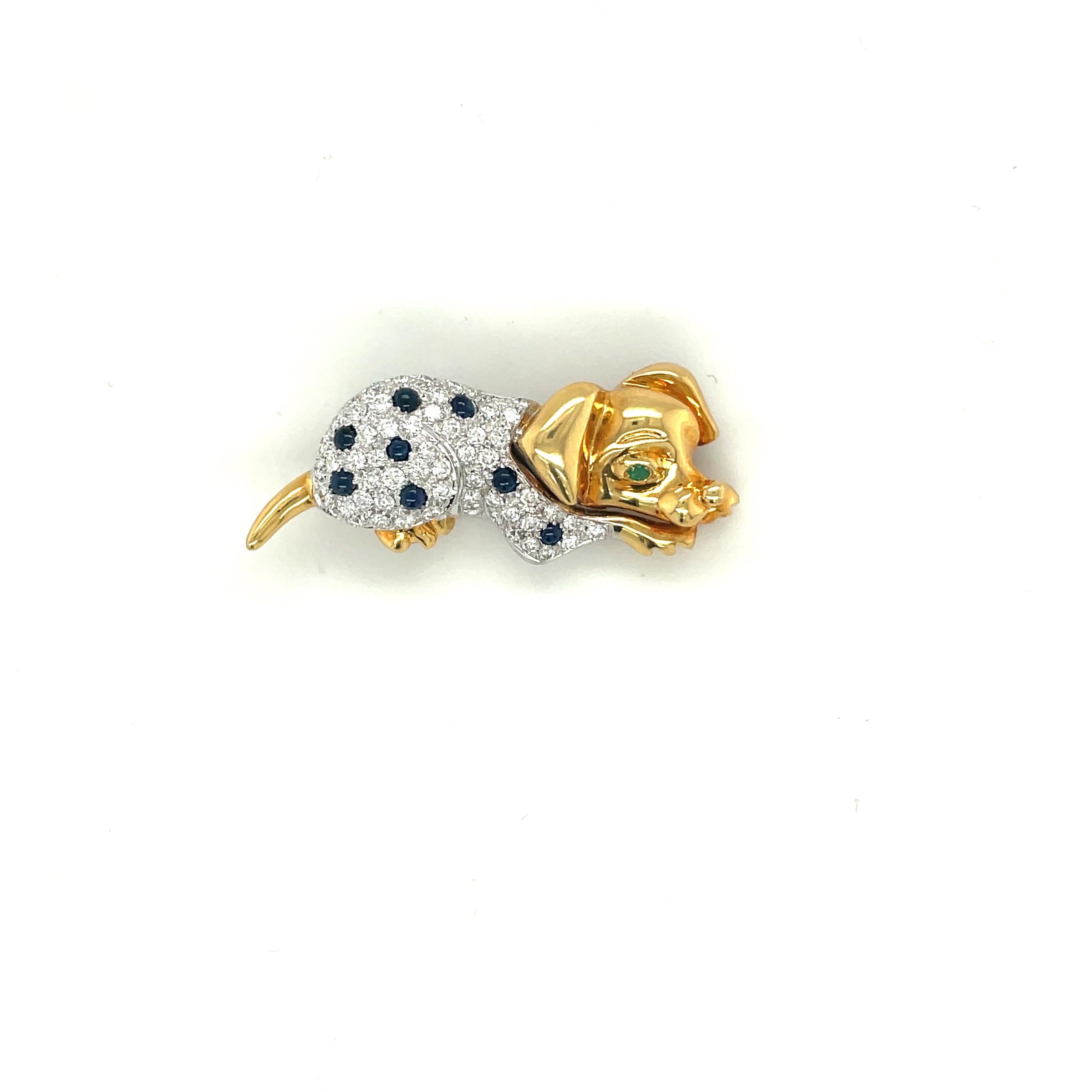 18 karat gold brooch designed as a dalmatian  sleeping dog  The white gold body is set with pave diamonds and scattered cabochon blue sapphires. The head and paws are shiny yellow gold and the eye is set with a round emerald.
Diamond weight 0.98