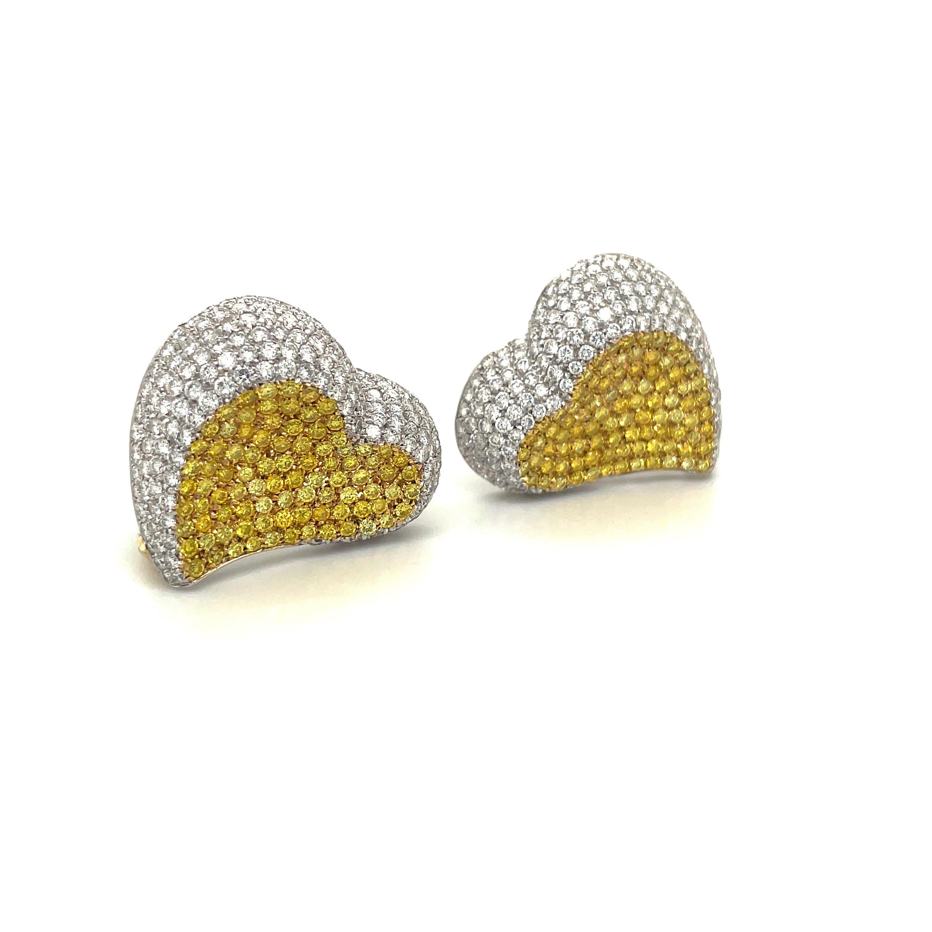 These beautiful large diamond heart earrings are comprised of 3.81cts of brilliant white diamonds, pave set in 18kt white gold, surrounding 2.35cts of fancy intense yellow diamonds pave set in 18kt yellow gold. They measure approximately 1