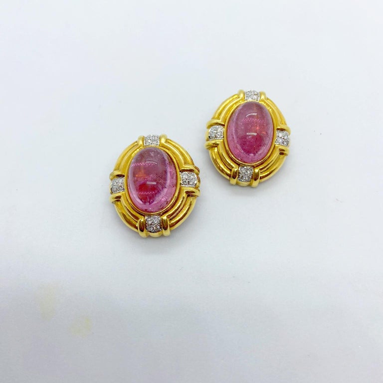 Classic 18 karat yellow gold clip on earrings, centering cabochon oval Pink Tourmalines and round brilliant Diamond accents. The earrings measure 1