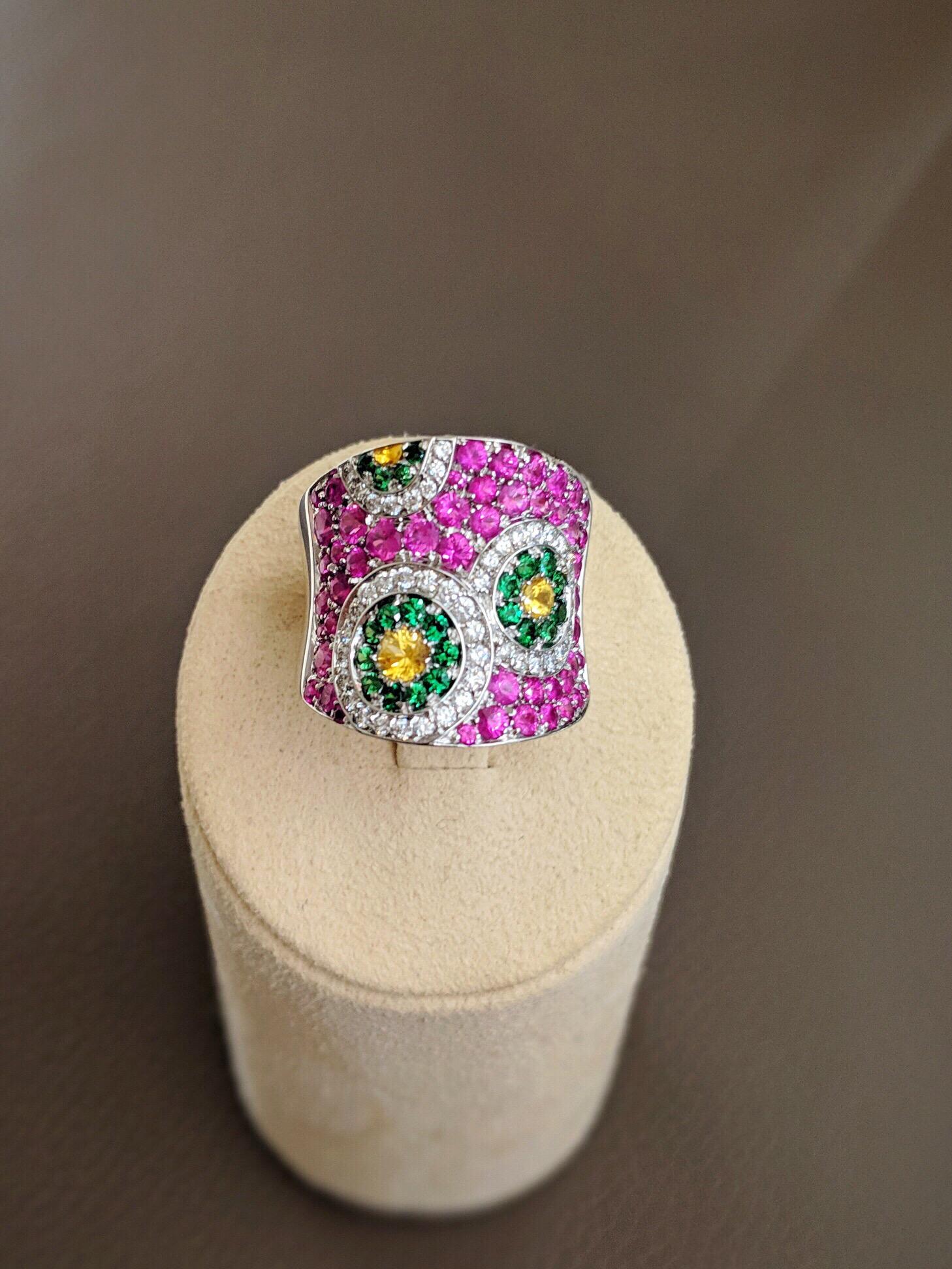 This Cellini Jewelers ring features a Kaleidoscope of white diamonds, yellow sapphires and Tsavorties which are set within a pink sapphire concave shaped ring. Set in 18 karat white gold. 
This whimsical design is part of the exclusive collection