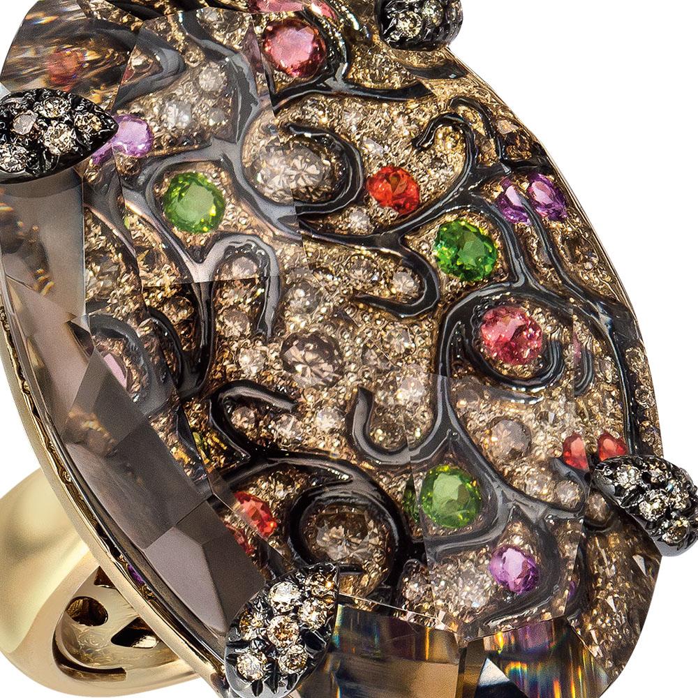 1.42 carats of round brown diamonds are precisely set with black enamel, tourmaline, amethysts and orange sapphires to create a beautiful arabesque design. This detailed piece is overlayed with a 39.70 carat brown quartz that magnifies the design