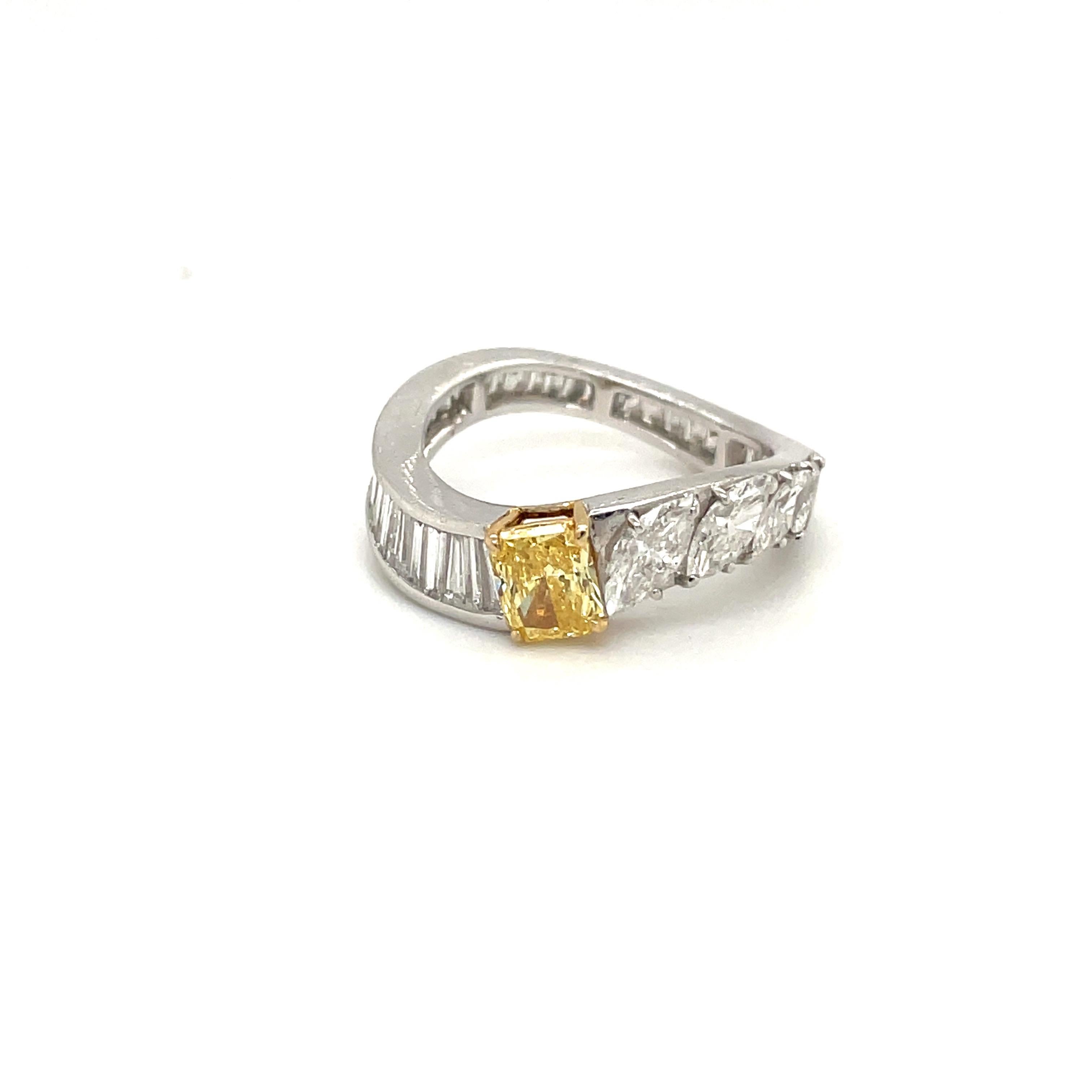 This unique 18 karat white gold ring is set with a GIA certified Fancy Intense Orange Yellow, VVS2 radiant cut center stone. The curvy  shaped band is set with diamond baguettes on on side and 5 marquise cut diamonds on the other. The baguette