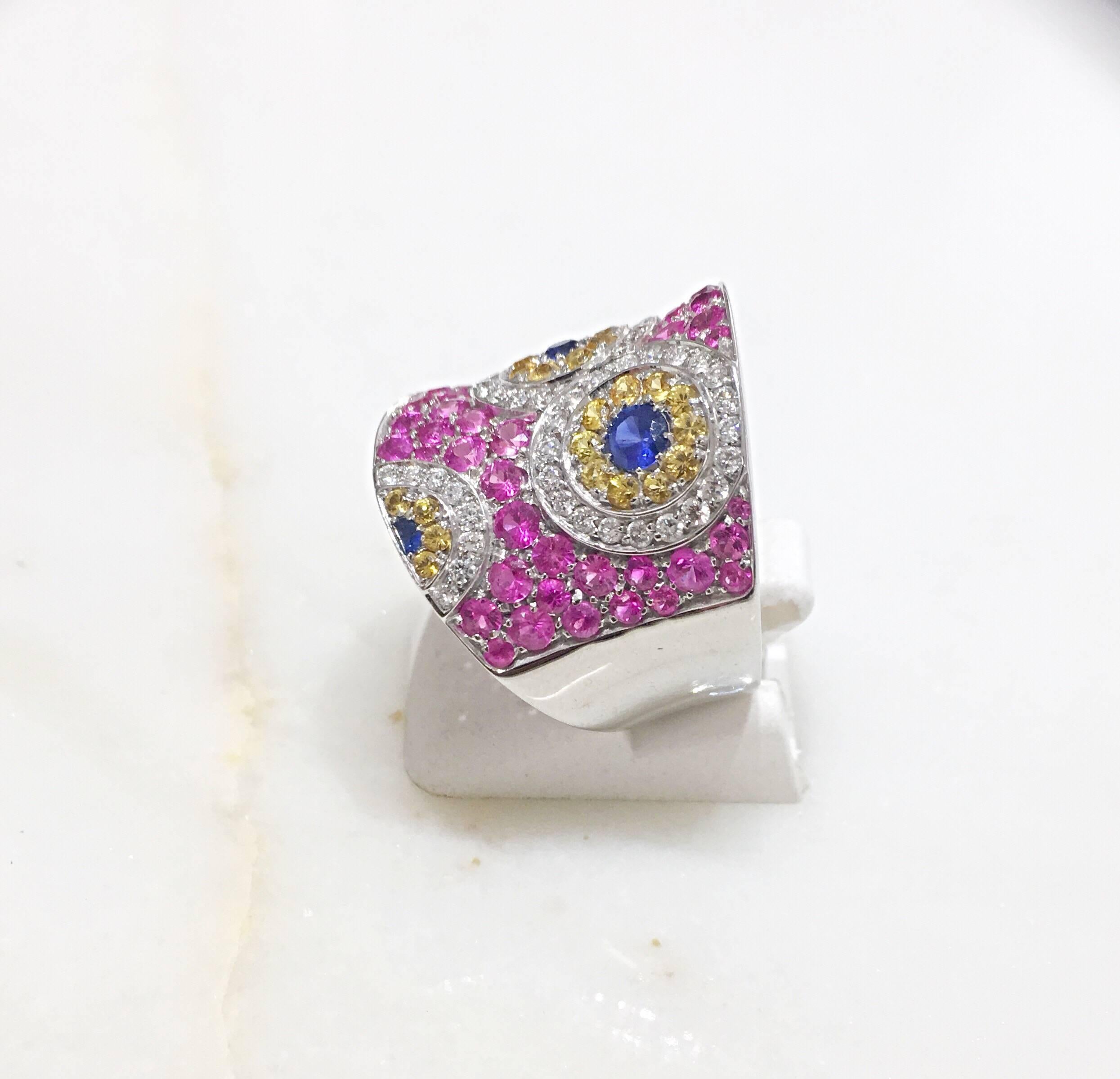 This Cellini Jewelers ring features a Kaleidoscope of white diamond, yellow and blue sapphires which are set within a pink sapphire concave shaped ring. Set in 18 karat white gold. 
This whimsical design is part of the exclusive collection created