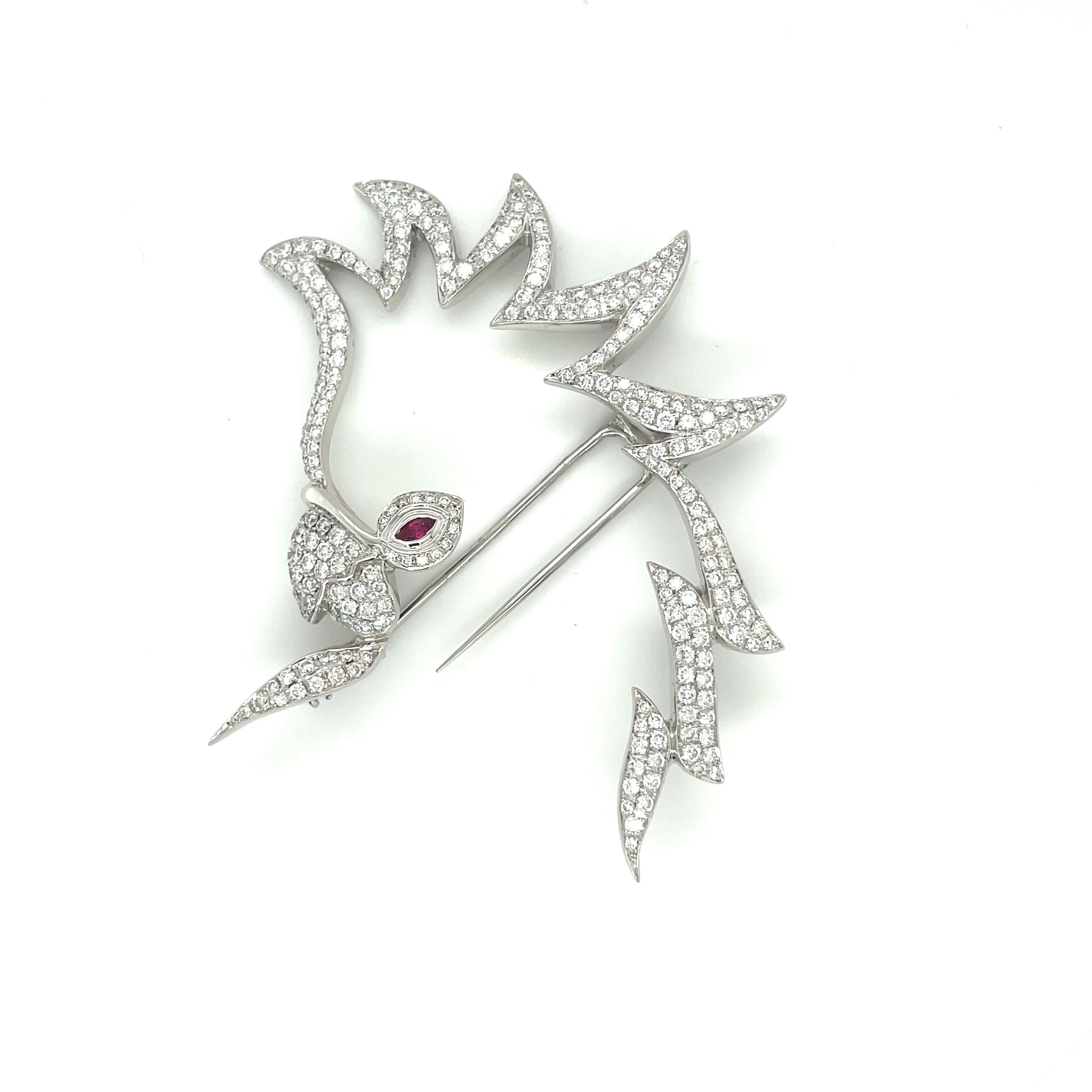 A graceful cockatoo silhouette in 18 karat white gold set with round brilliant diamonds. The  cockatoo's eye is a marquise shaped ruby. The open worked brooch measures 2.75