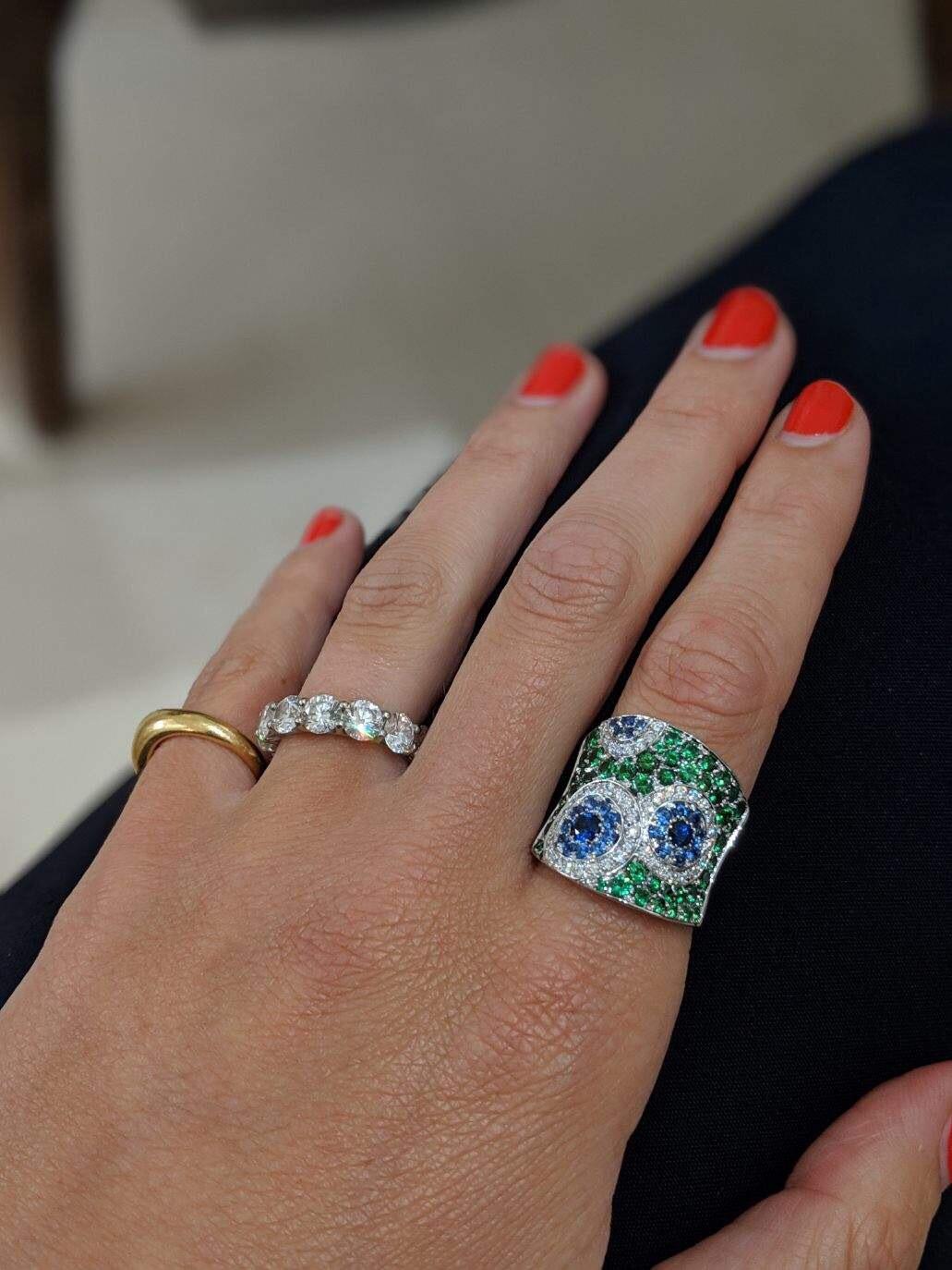 Dieser Ring von Cellini Jewelers zeigt ein Kaleidoskop aus weißen Diamanten und blauen Saphiren, die in einen konkav geformten Ring aus grünem Tsavorit eingefasst sind. Fassung aus 18 Karat Weißgold. 
Dieses skurrile Design ist Teil der