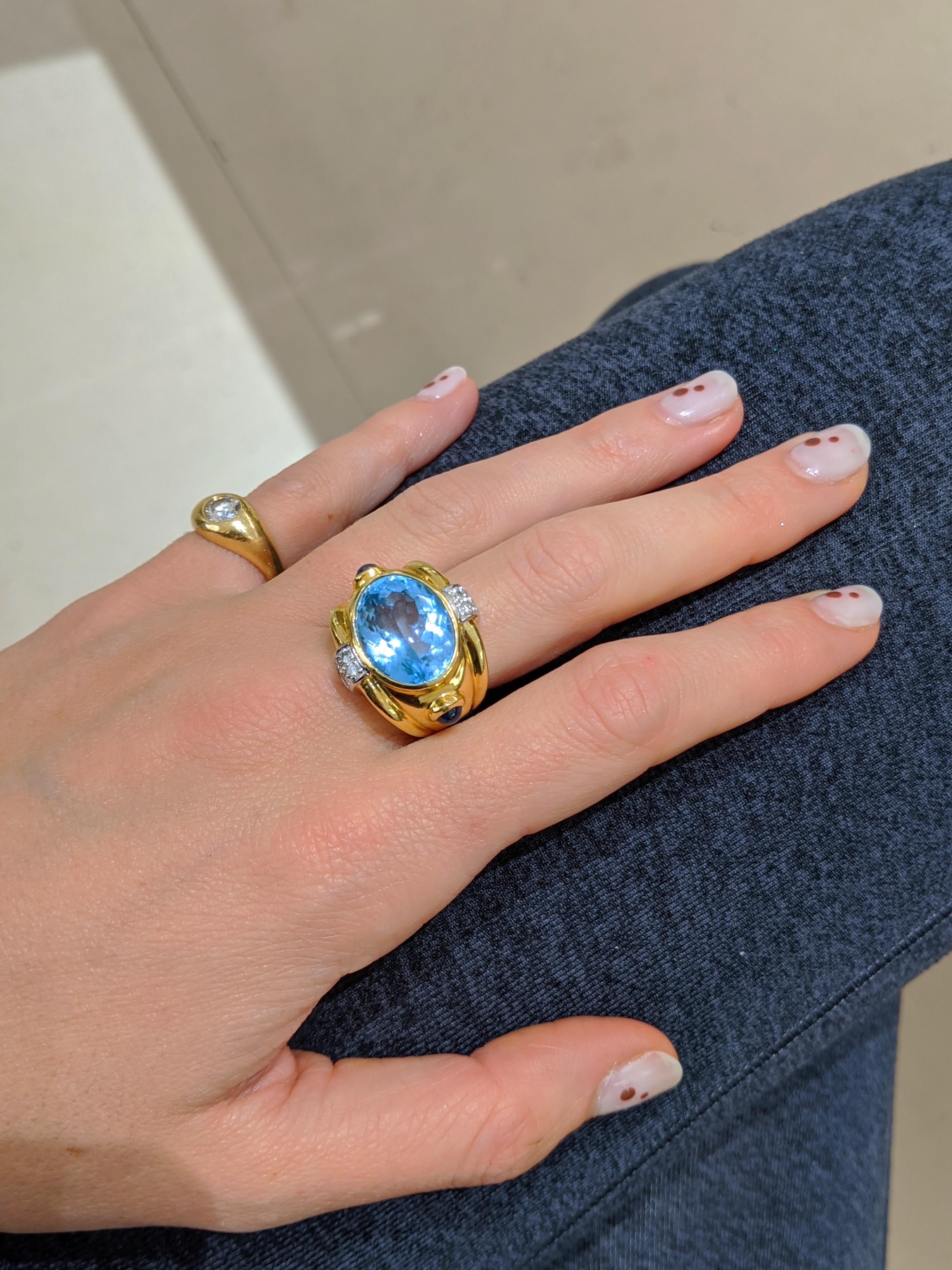 This beautiful 18kt. gold ring Designed by Cellini Jewelers NYC, features a 12.23Ct. Blue Topaz center with .23Ct. Diamond accents. The ring also features two cabochon sapphire detailing. 
Ring is stamped 18kt and 750. 
Ring size 6.75, May be able