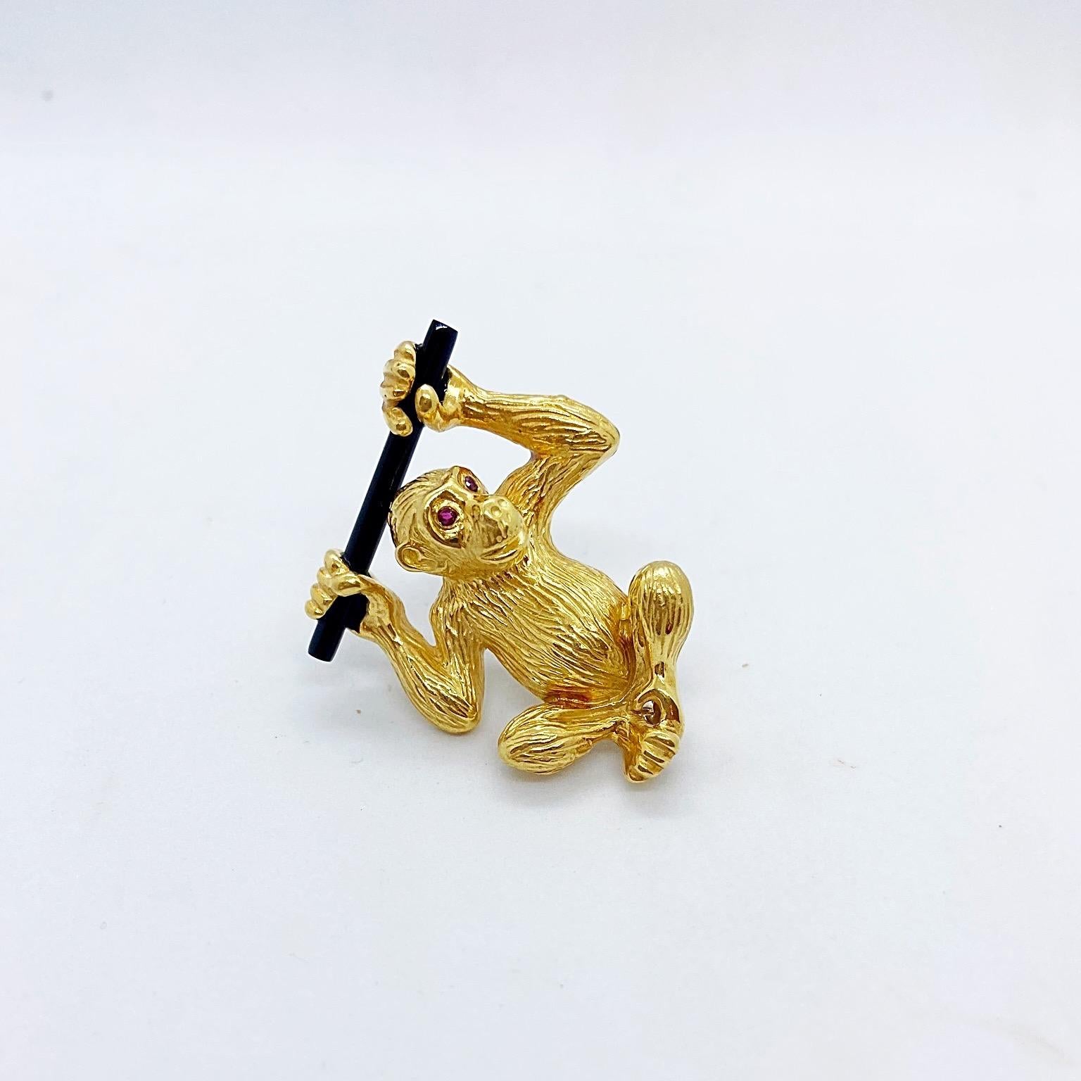 Un adorable singe en or jaune 18 carats, aux yeux de rubis, est suspendu à une branche d'onyx noir. La broche mesure 1,5