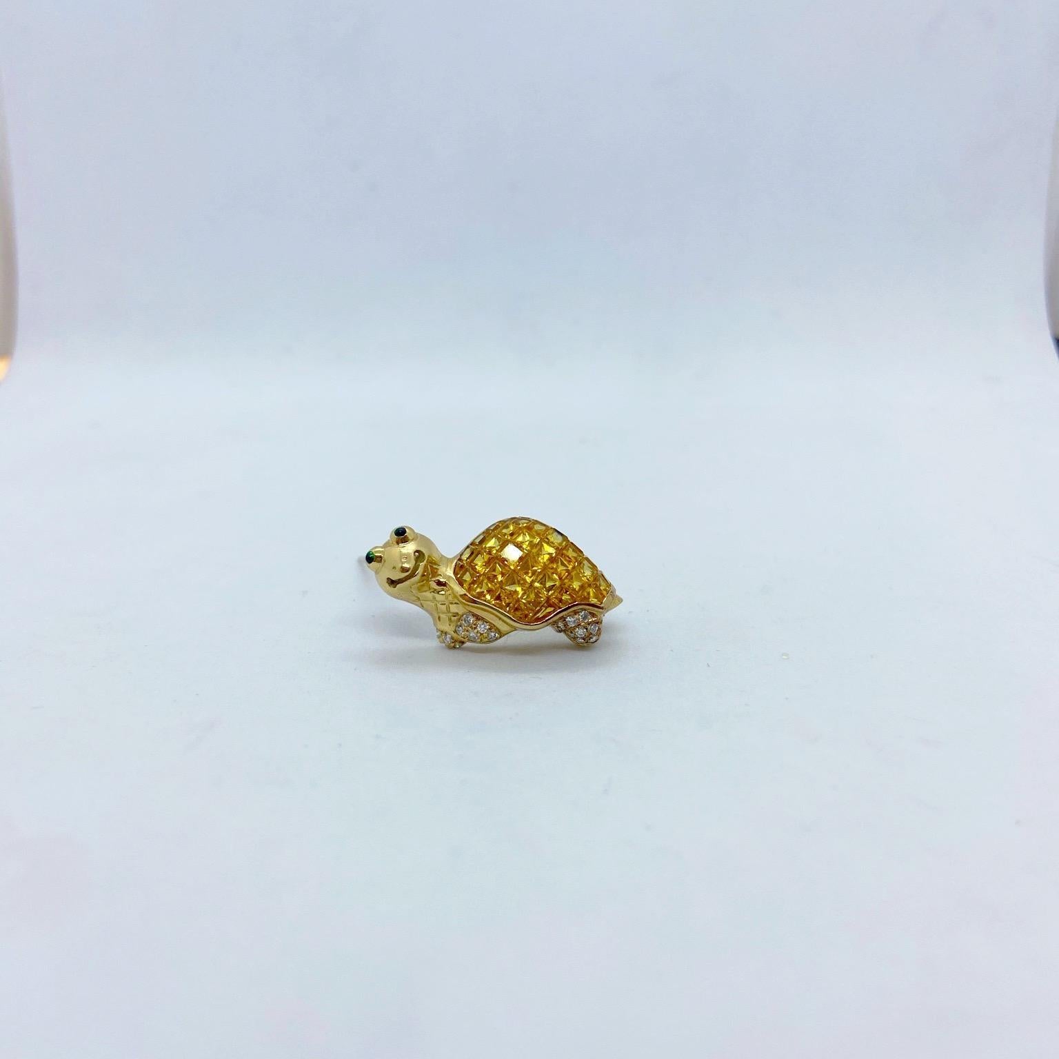A beautifully crafted turtle brooch. The turtle shell has been invisibly set with square cut yellow sapphires. His feet are set with round brilliant diamonds and his eyes are cabochon emeralds. He is a polished 18 karat yellow gold with a big smile.