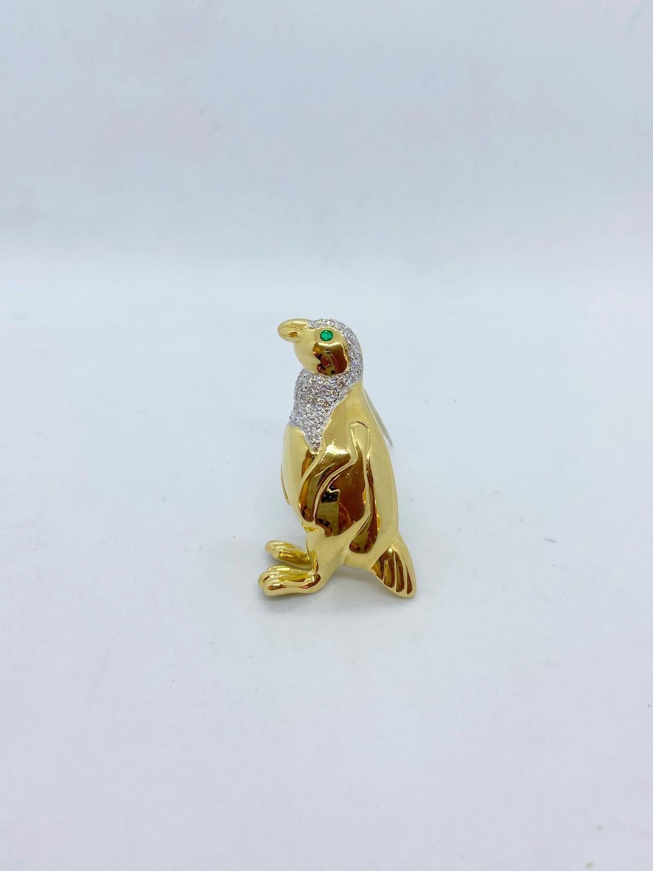 A large 18 karat yellow gold penguin brooch. The penguin is beautifully crafted in a high polished yellow gold. His neck and head are set with round brilliant diamonds in white gold. His eye is a round emerald. The penguin measures 1-7/8