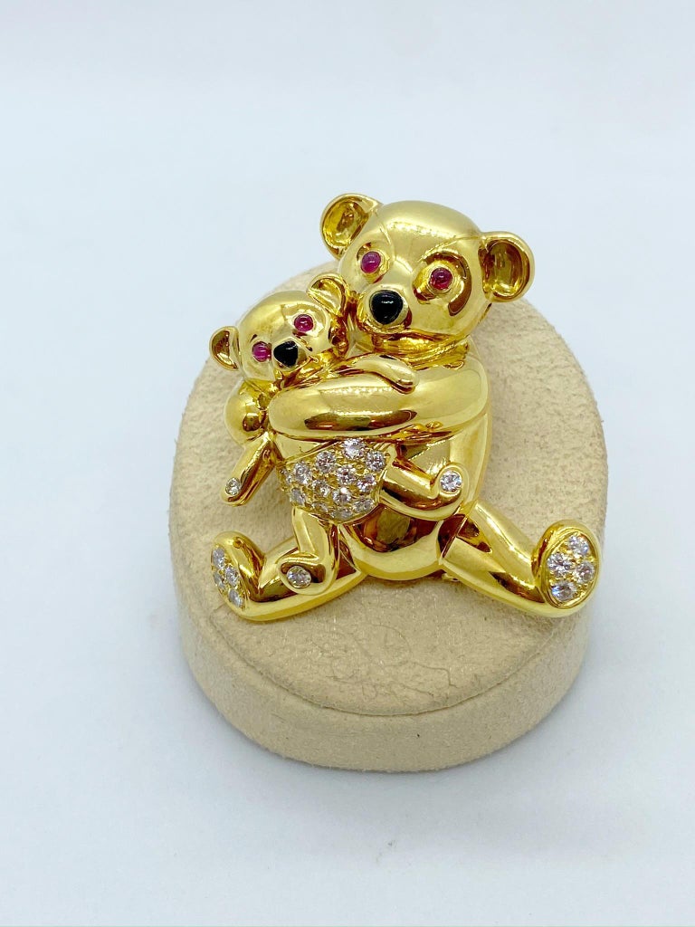 A big hug is the best way to describe this beautifully detailed 18 karat yellow gold teddy bear brooch. The mama and the baby are crafted in a hi polished yellow gold with diamond accents and ruby eyes. Black onyx is set for their noses. The brooch