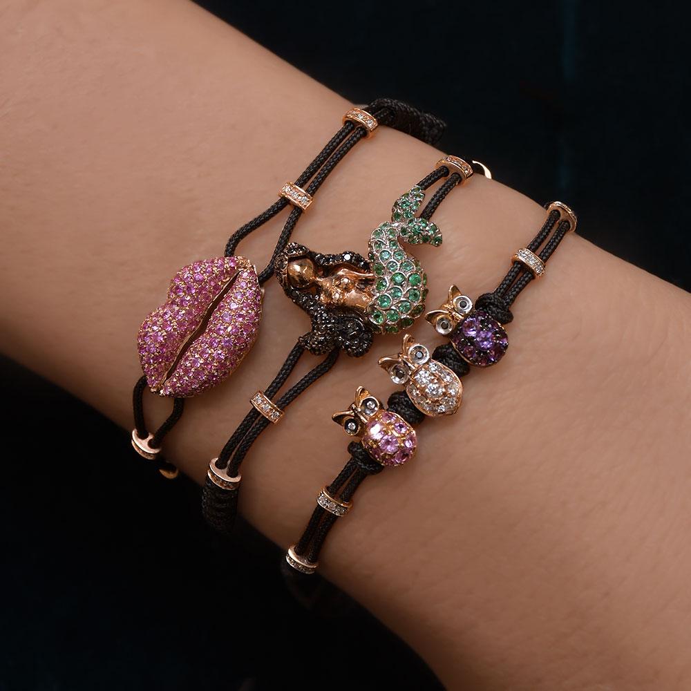 Known to symbolize wisdom,femininity, and fertility, this lovely Pippo Perez 18kt rose gold 3 Owl bracelet is set with Diamonds .20cts., Pink Sapphires .20cts., and Amethyst .19cts.
It is strung on a black nautical adjustable cord. 
Each owl
