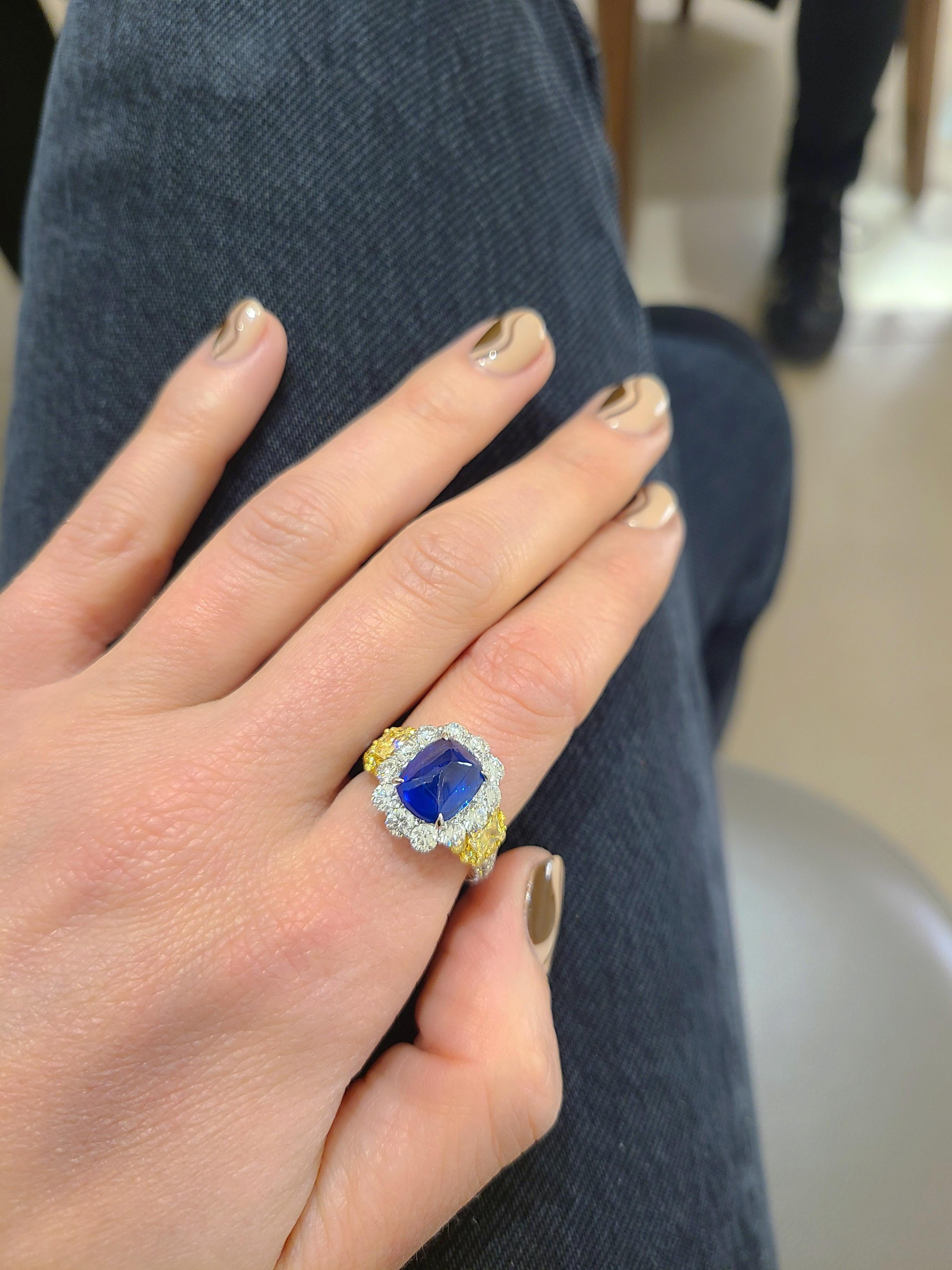 This exquisite center stone platinum ring features a sugarloaf cabochon blue sapphire as the main attraction. Round white brilliant diamonds surround the sapphire . Set on either side are fancy yellow trapezoid side stones which are bordered in