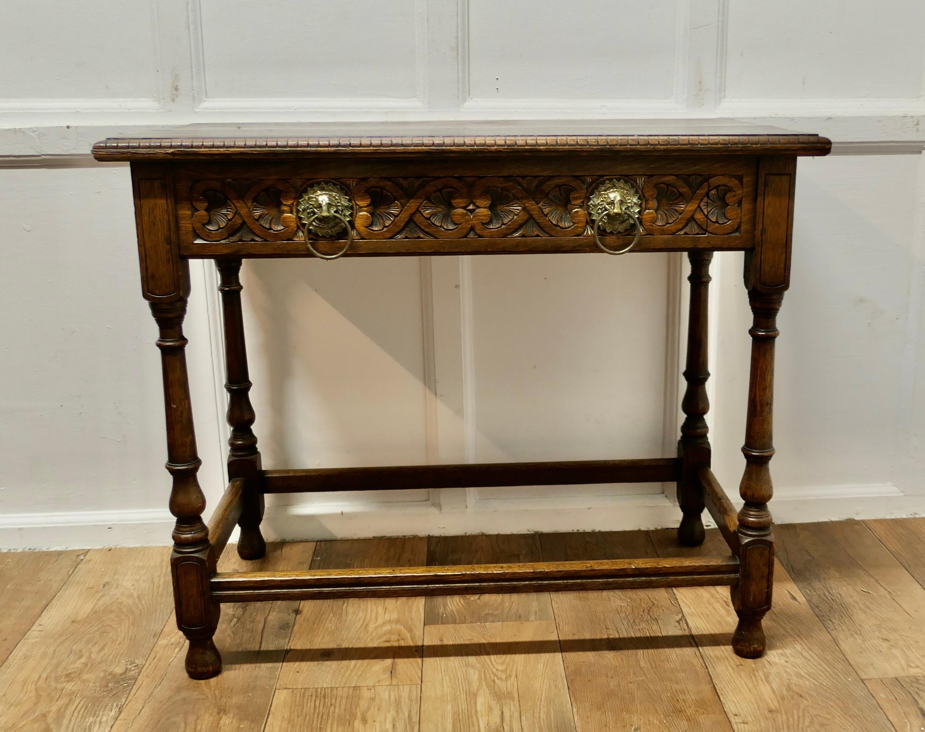 Celtic Carved Oak Occasional Table
 
A particularly fine quality Occasional Table, it has a dentil carved detail along the top edge and a long drawer which has Celtic carving along the front and is set with 2 stunning Lion’s mask ring handles which