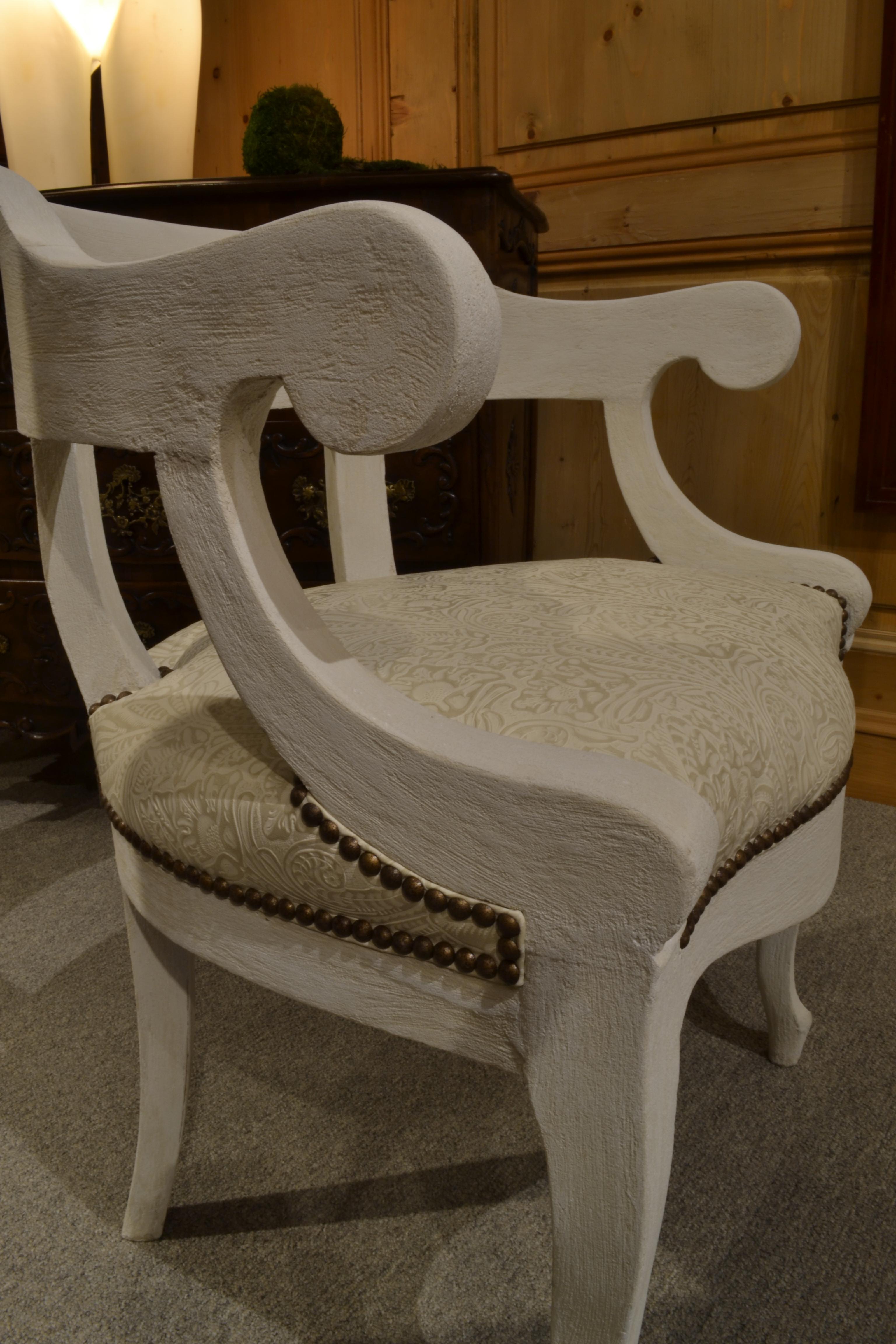 This comfortable armchair has a low, curved back and a saddle seat. Nailheads frame the seat. It is lightweight in solid wood with a subtle but noticeable cement texture.