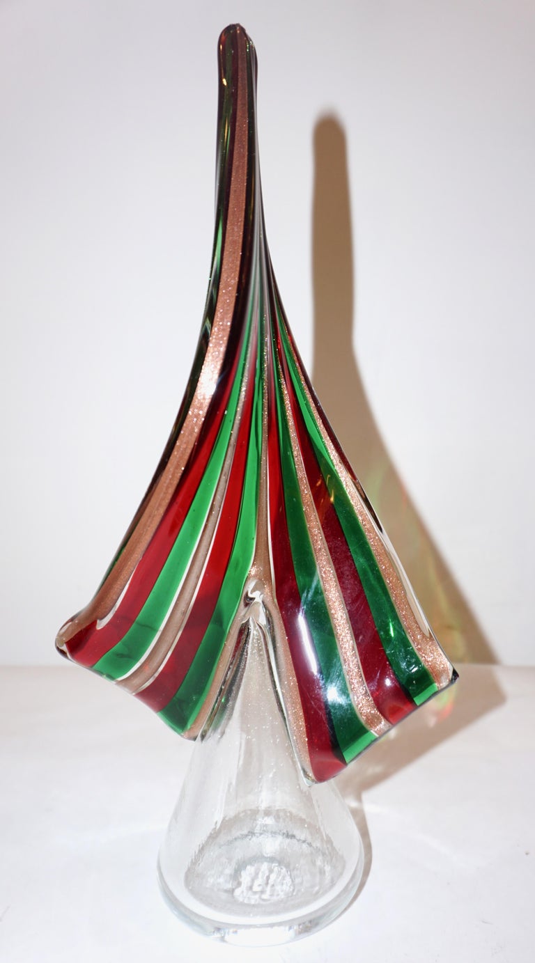 A unique Minimalist sculpture, as a Christmas Tree, in a very modern organic sleek design, a collectible piece, mouth-blown and entirely handcrafted in Murano Italy, in crystal clear glass decorated with stripes of murrine in crimson red, green and