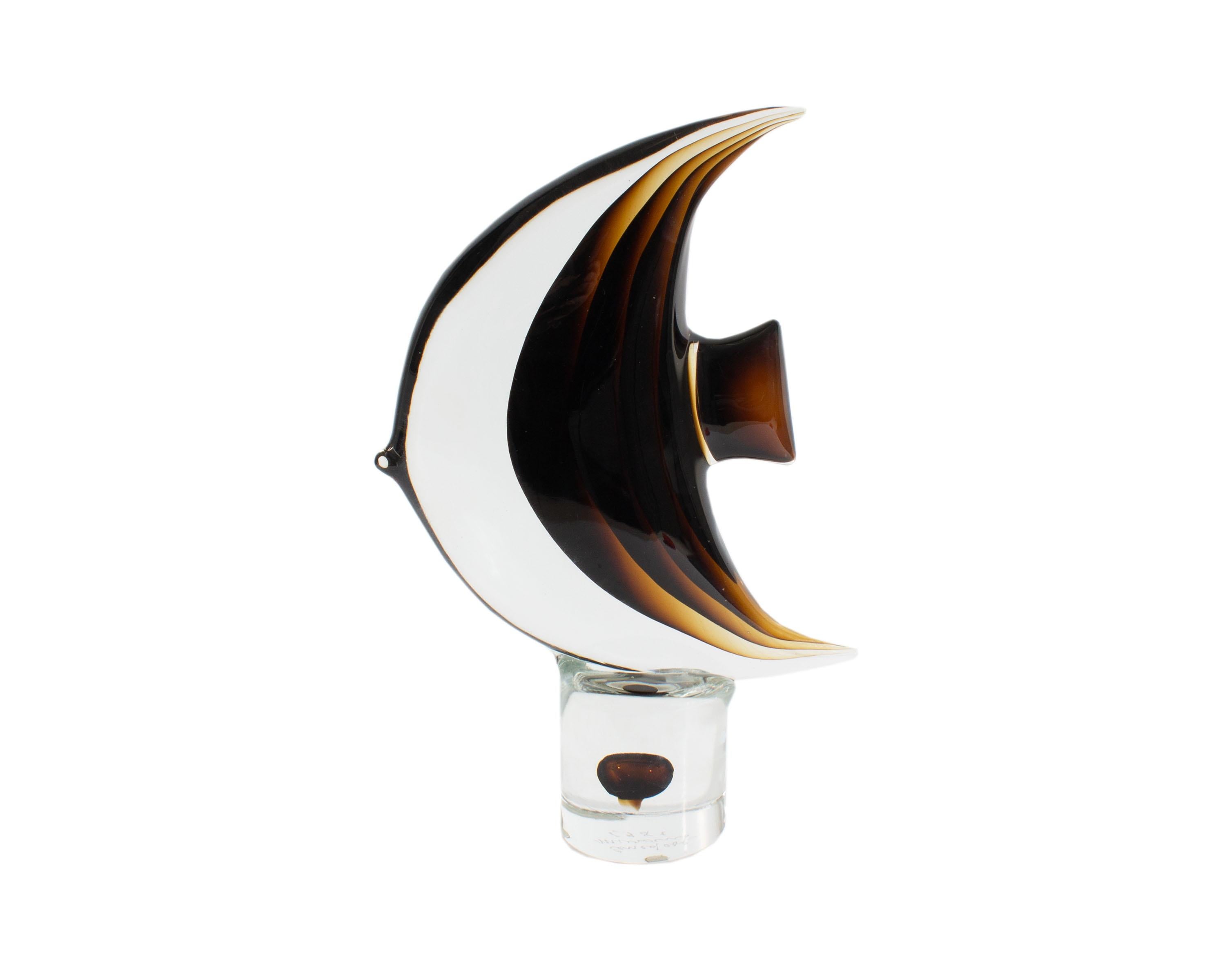 A 1981 art glass fish sculpture by Cenedese Murano. Made in Italy, the abstract sculpture resembles a tropical fish upon a cylindrical base. Gradient brown and transparent glass form the body of the fish. A brown orb floats within the center of the