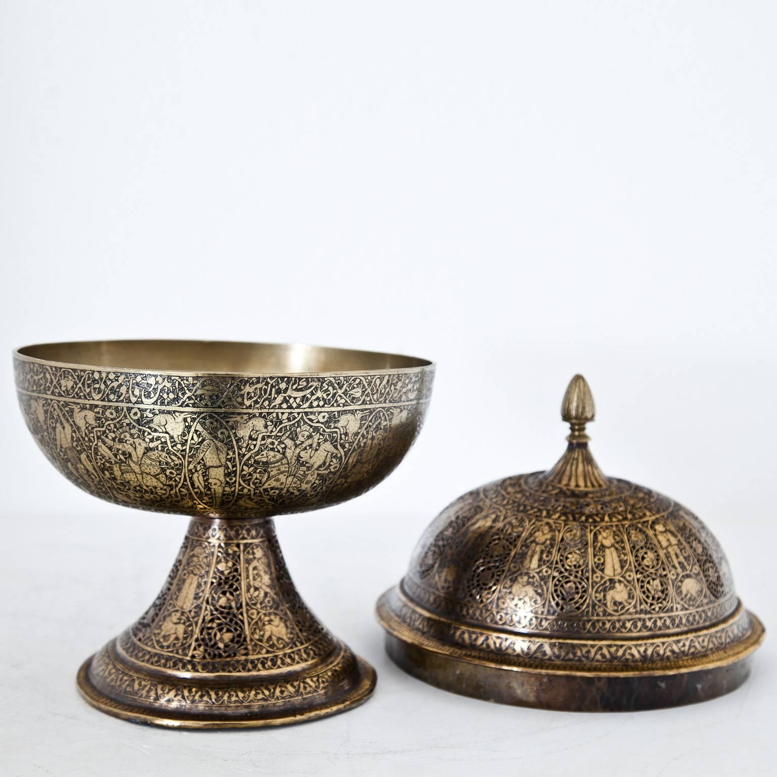 Persian brass censer with round cuppa and a lid with cut-outs. The wall depicts humans and animals in medallions. The cup shows a revolving Arabic inscription.