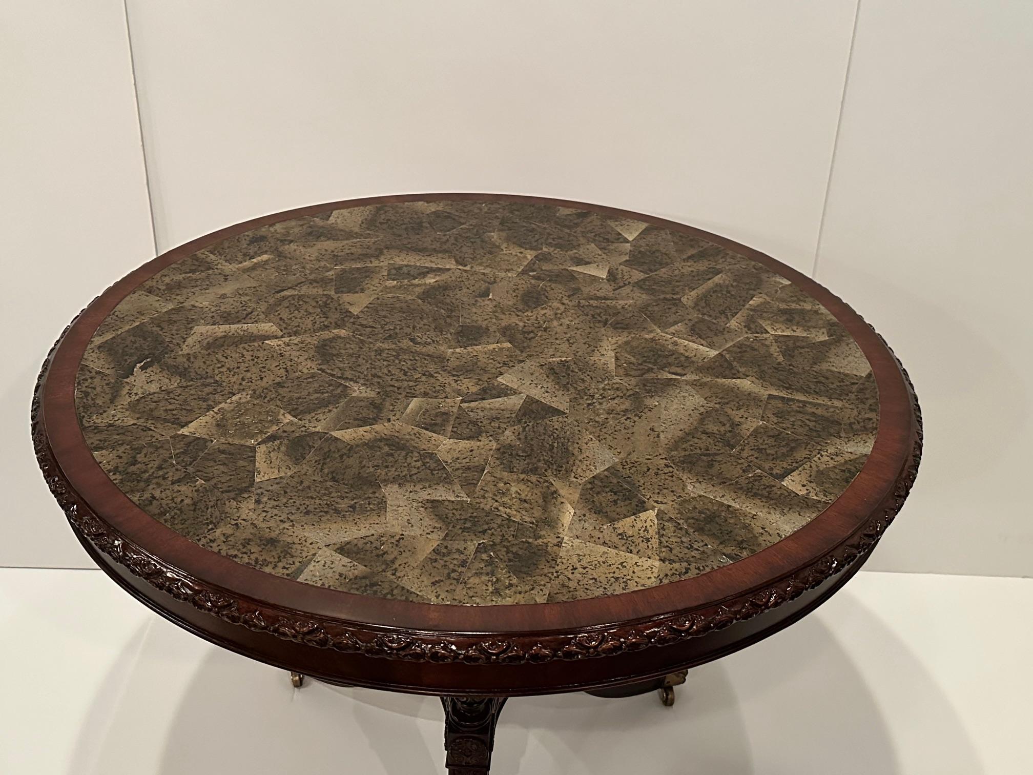 Stunning round center table having carved mahogany trio of splayed legs with center decorative urn.  Top is a fascinating lacquered coconut shell that takes on the appearance of natural stone or marble.
apron 28”