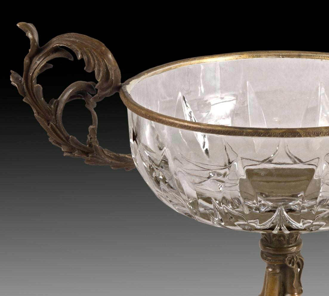 Centerpiece in bronze and glass.
Lost wax casting of bronde.
It is cup-shaped, with the base made of four bamboo canes joined with a cord and decorated with flowers and leaves, the transparent glass container and the two handles with inward curved