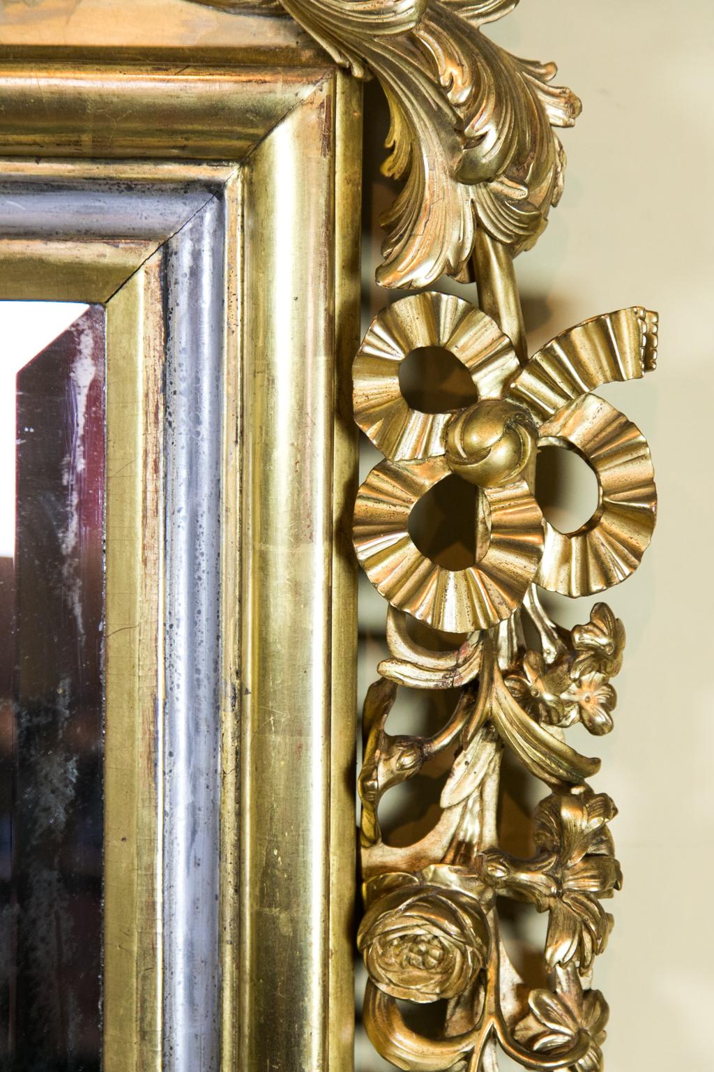 Central European carved gilt mirror is richly carved with floral arabesques and a painted crest with heraldic birds surrounding the painted crest with crown. The mirror has 1.25” bevel and is framed with carved gilt ribbons and flowers.
   