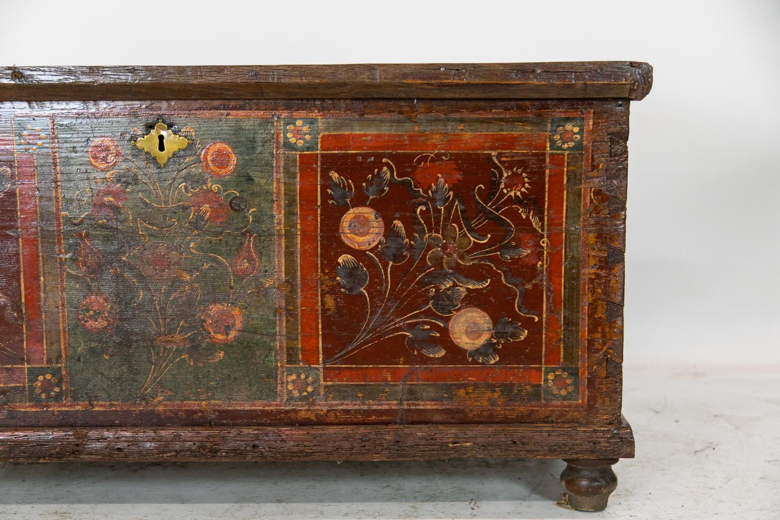 This Central European painted blanket chest has three floral painted panels on the front and large exposed dovetail construction on the front and back corners. The sides have the original red paint and the top is natural pine. The interior has 19th