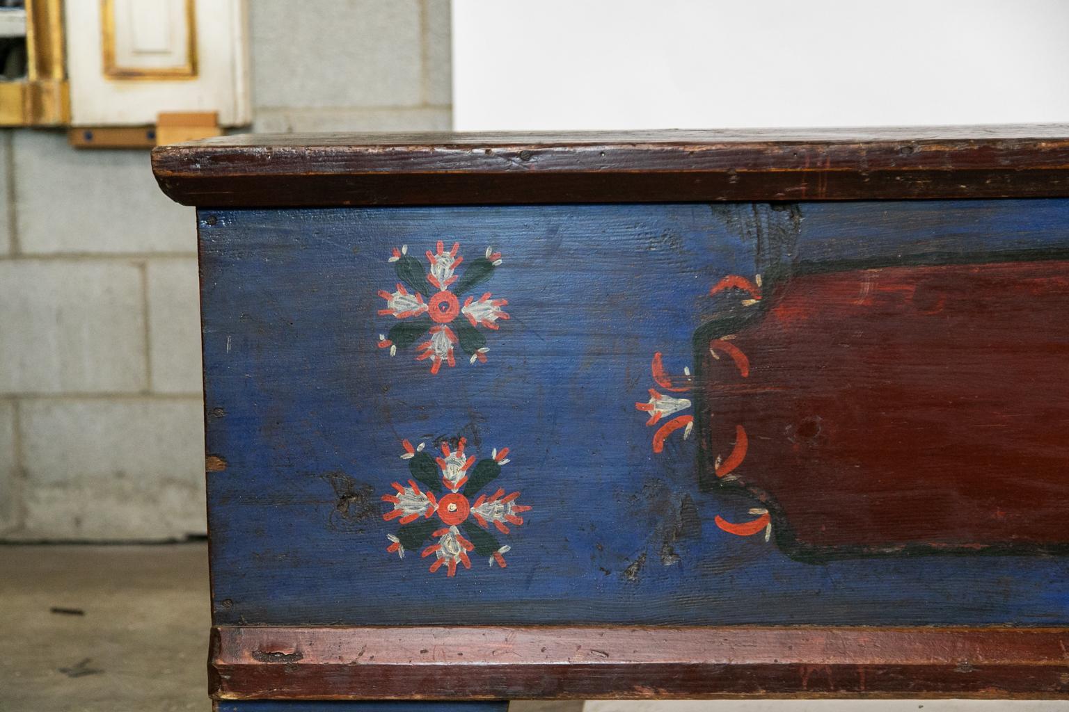 This blanket chest has painted floral decoration on the front. There are traces of the original paint on the top which has mostly worn through to the original pine surface. The interior has three divided compartments with exposed large dovetail