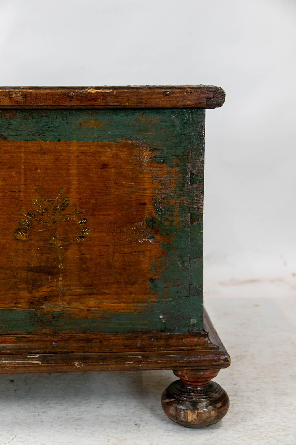 The front and top of this blanket chest have the original blue paint. There is exposed dovetailed construction on the sides that terminate in the original bun feet.