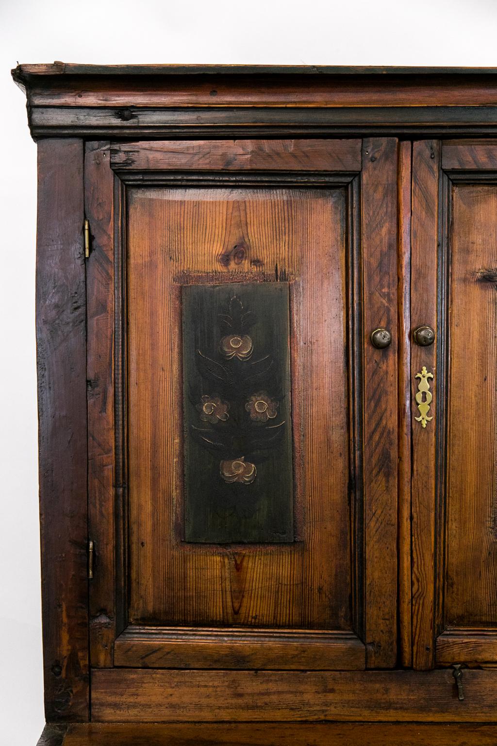This Central European step back cupboard is made of heart pine. The upper and lower doors have raised panels painted with floral designs and framed with shaped molding. The construction has large exposed dovetails and exposed mortise and Tenon
