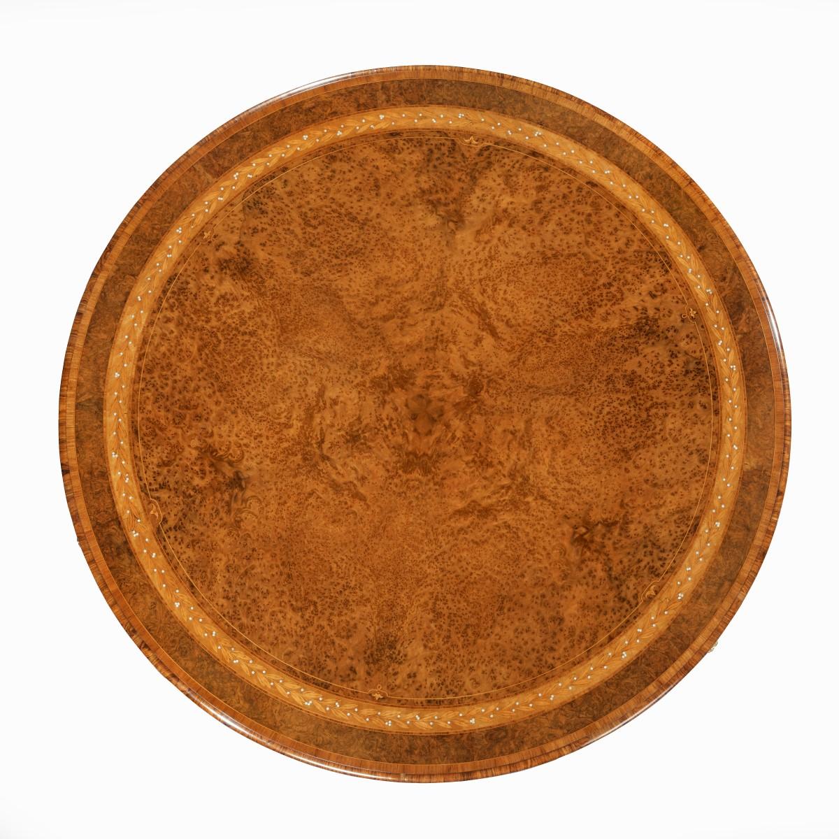A centre table attributed to Holland and Sons related to a table in Clarence House, this exceptional table has a circular top decorated with six radiating amboyna veneers with a border of concentric marquetry rings. The decoration comprising