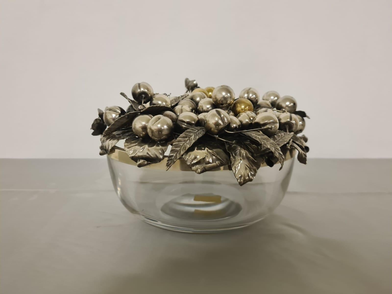 Pièce maîtresse en argent.

Centre de table raffiné avec couvercle en argent.

Cet élégant objet décoratif se compose d'un grand bol en verre avec un bord argenté.

Le couvercle, quant à lui, est entièrement en argent et se compose de feuilles, de