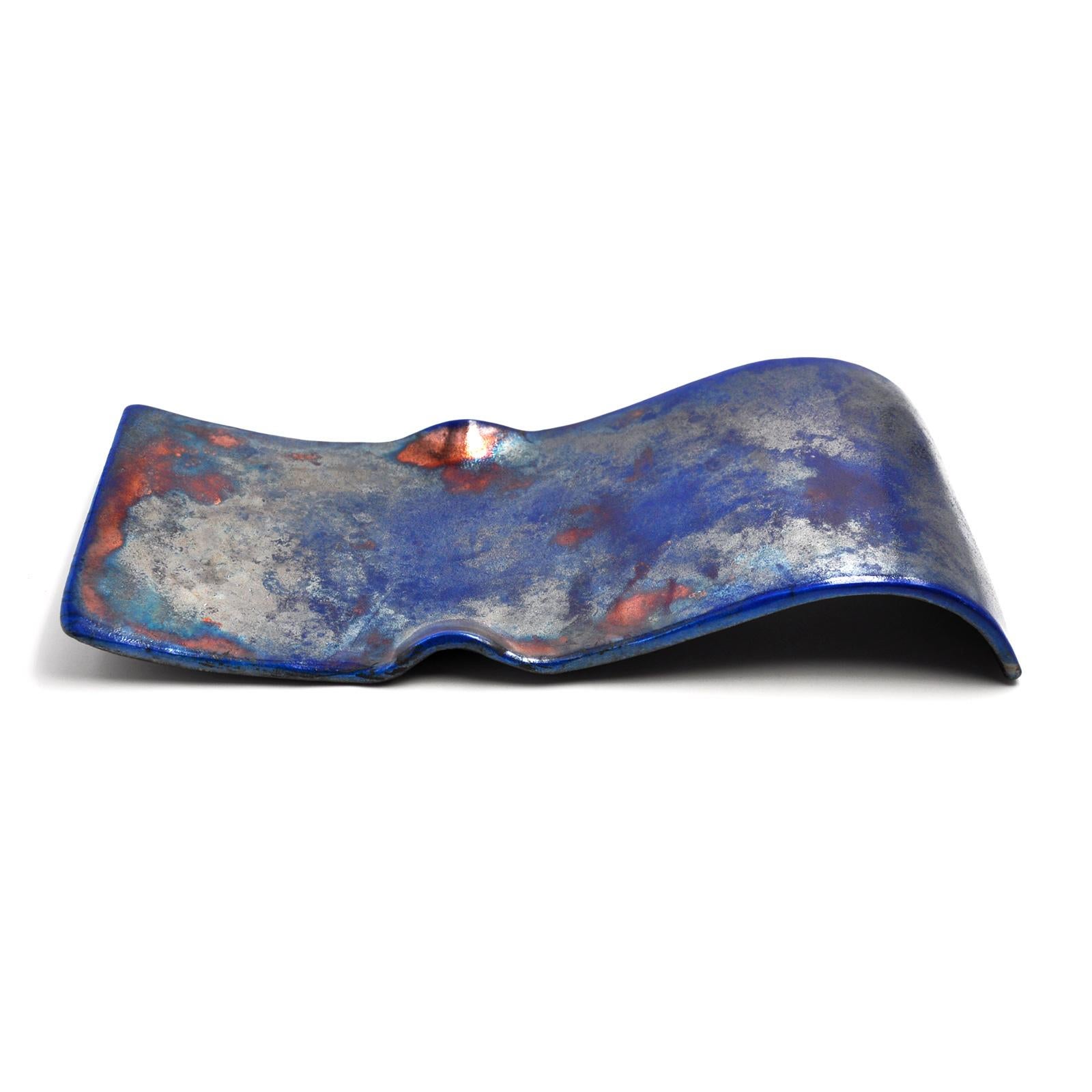 Modern, linear design and the warm  luster of the decoration, make  SILVER BLUE SMALL WAVE  a centerpiece of  strong personality.
Designed and  modeled entirely by hand by designer-artist Nino Basso, this elegant decorative plate  is made of raku