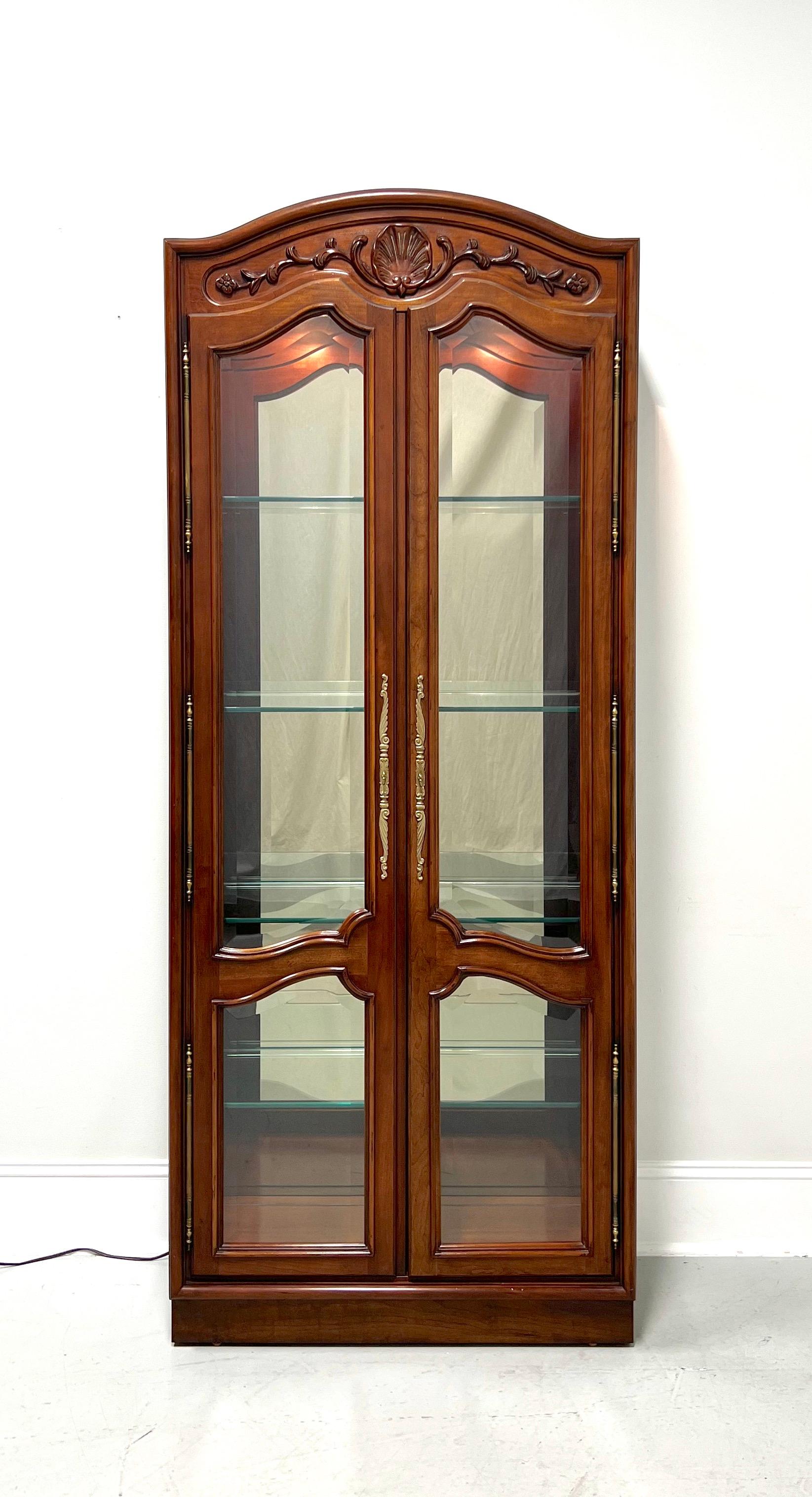 A French Provincial style curio cabinet by Century Furniture, from their Chardeau Collection designed by Raymond K Sobota. Cherry wood with decorative brass hardware, dual arched glass front doors, arched glass side panels, carved top with shell